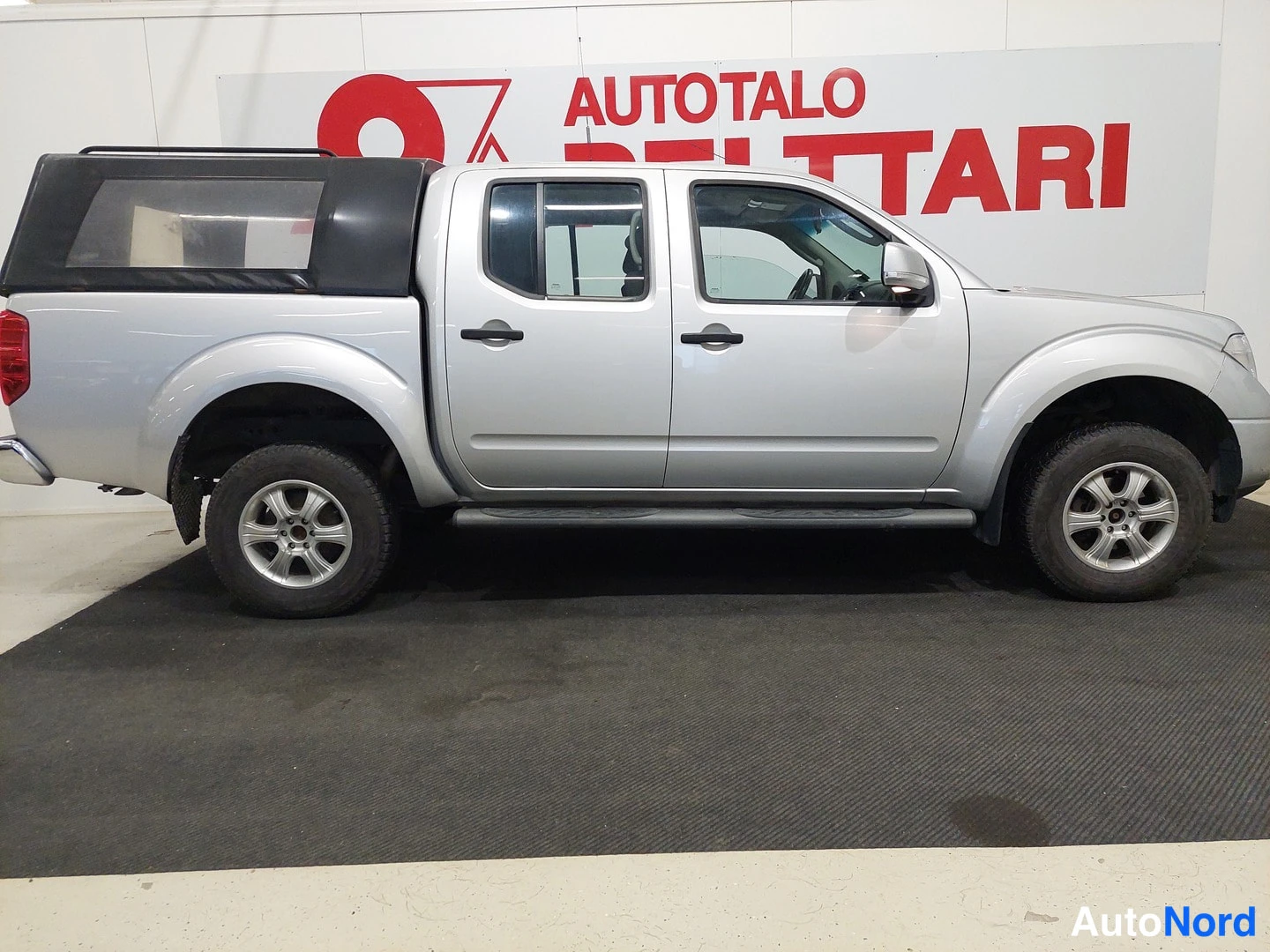 Sivulta: Hopeanvärinen Nissan Navara Double Cab -mallinen avolava-auto sivulta kuvattuna; autoon on asennettu musta lavakate.