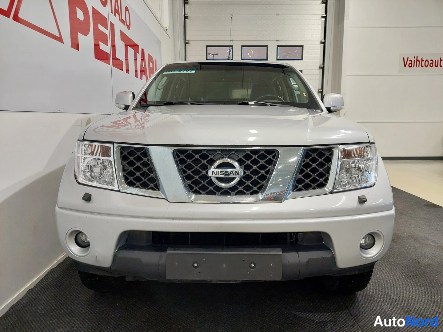 Edestä: Hopeanvärinen Nissan Navara suoraan edestä kuvattuna; kylkienetan, käännytyssuunnan vilkut ja etupuskurin sumuvalot näkyvät.