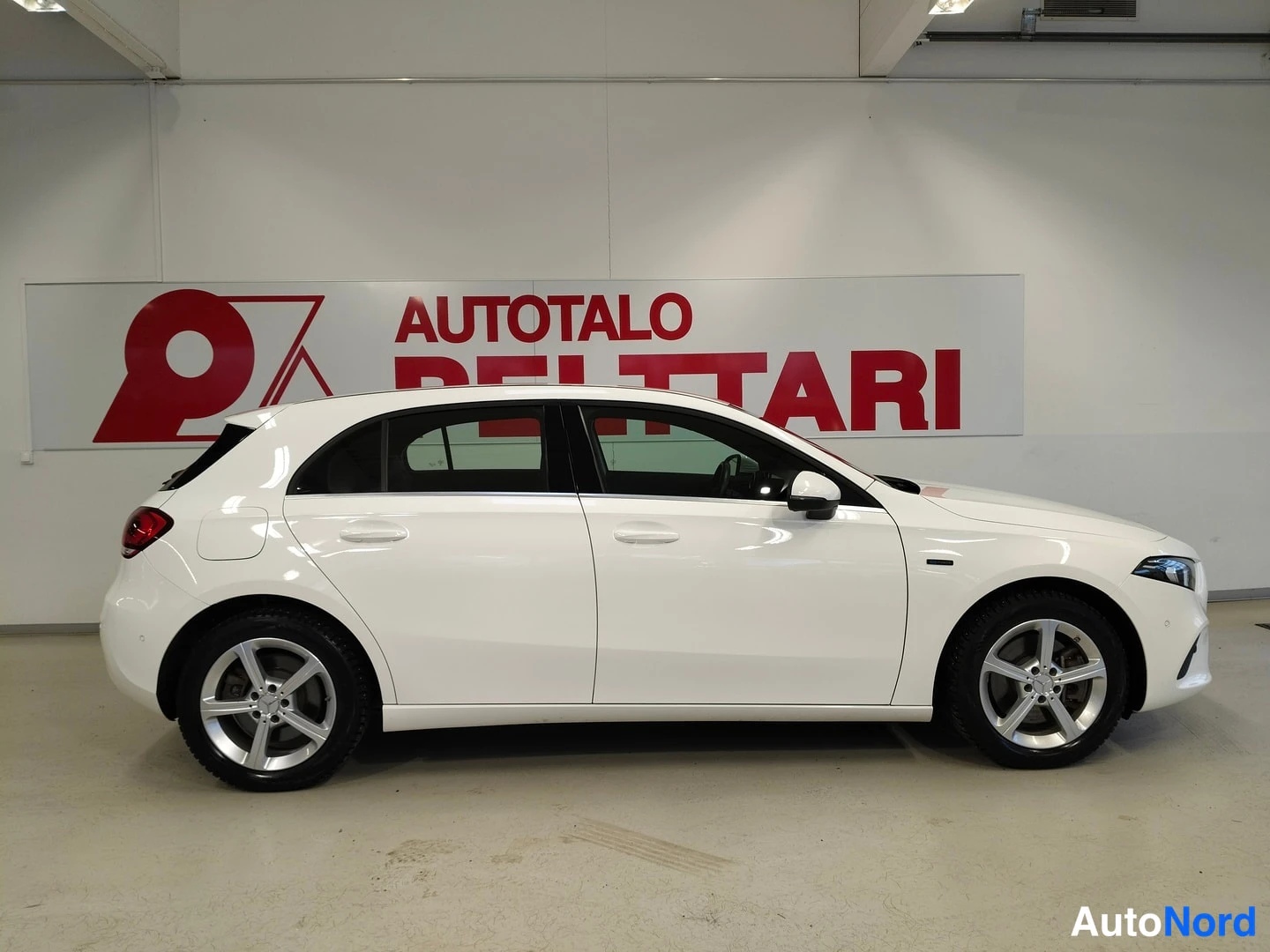 Sivulta: Valkoinen Mercedes-Benz A -hatchback sivuprofiili vasemmalta sisähallissa, hopeiset peltivanteet ja viistoperä.