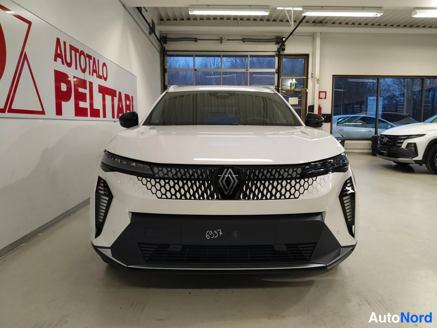 Edestä: Renault Scenicin keula suoraan edestä valkoisena, etusäleikkö ja Renault-merkki näkyvissä.