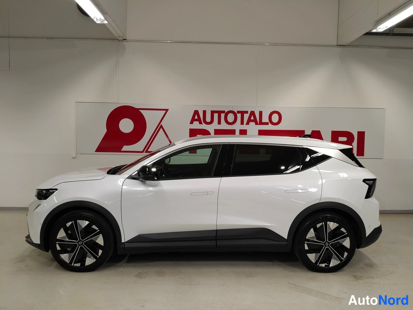 Sivulta: Renault Scenicin sivuprofiili valkoisena, vasen sivu ja pyörät näkyvissä sisätilassa.