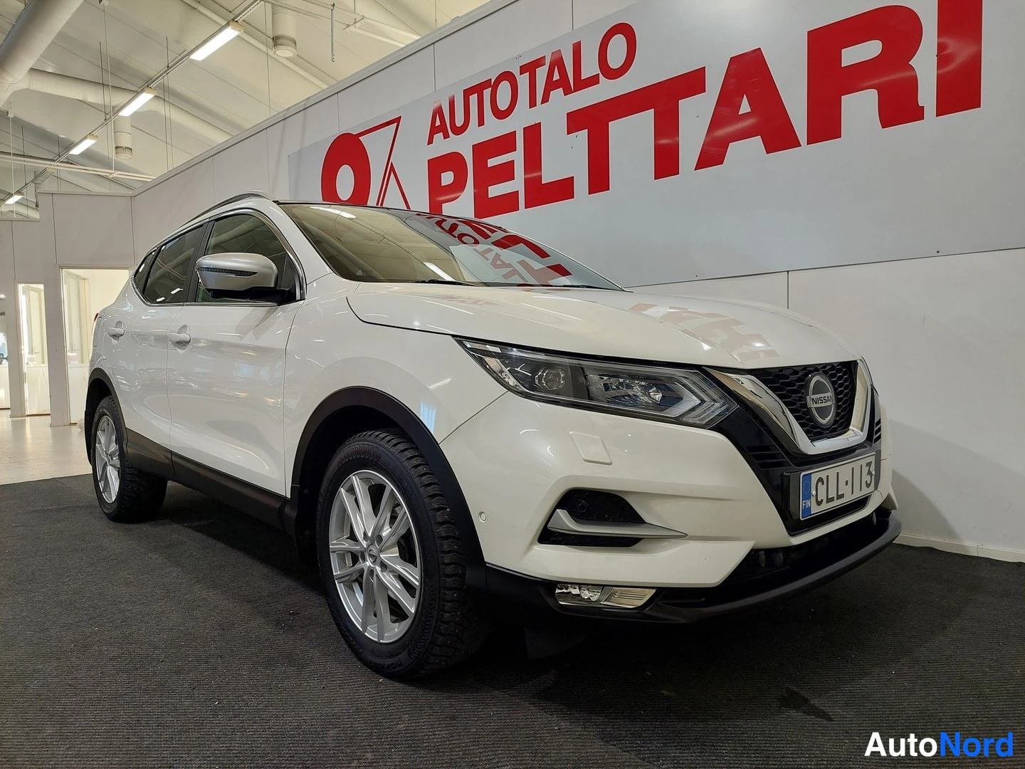 Etuviisto, nokka oikealle: Valkoinen Nissan Qashqai kuvattu etukulmasta oikealta sisätiloissa.