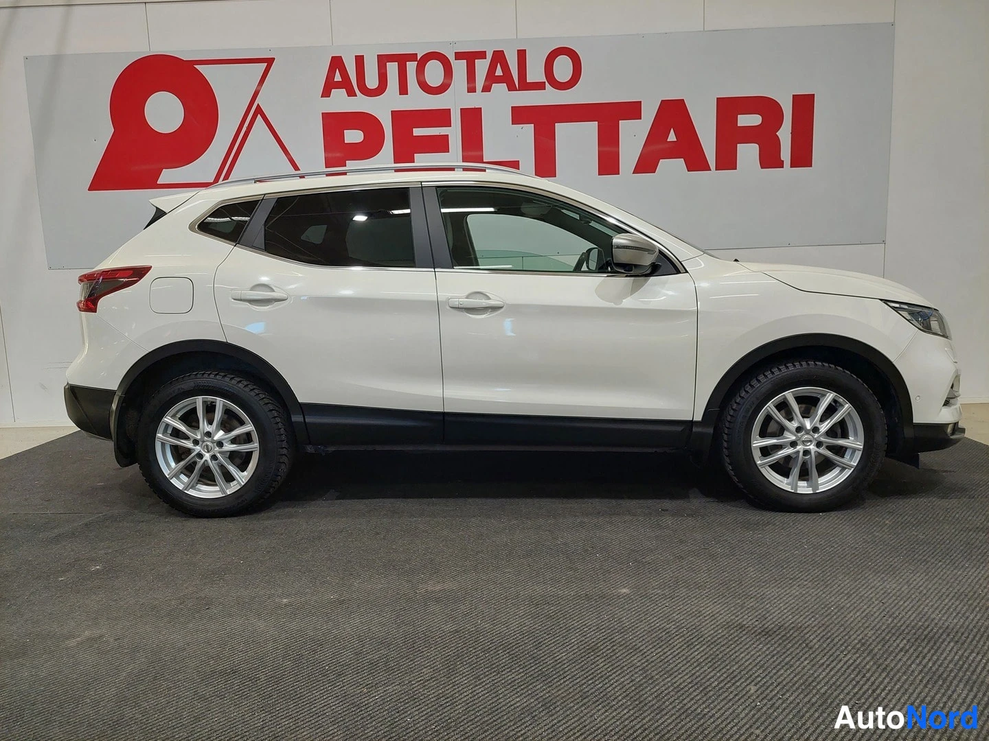 Etuviisto, nokka oikealle: Valkoinen Nissan Qashqai -maasturinen etukulmasta, keula oikealla, sivukulma sisätiloissa.