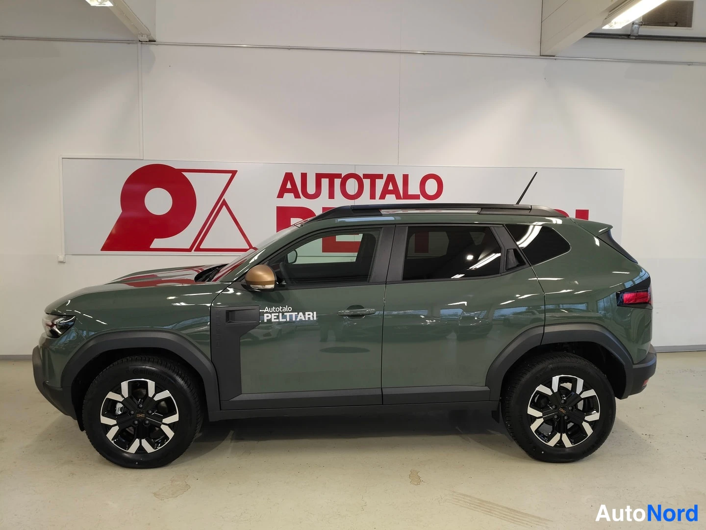 Sivulta: Vihreä hybridsuviauto sivulta kuvattuna sisätiloissa, oikea kylki ja pyörät näkyvissä.