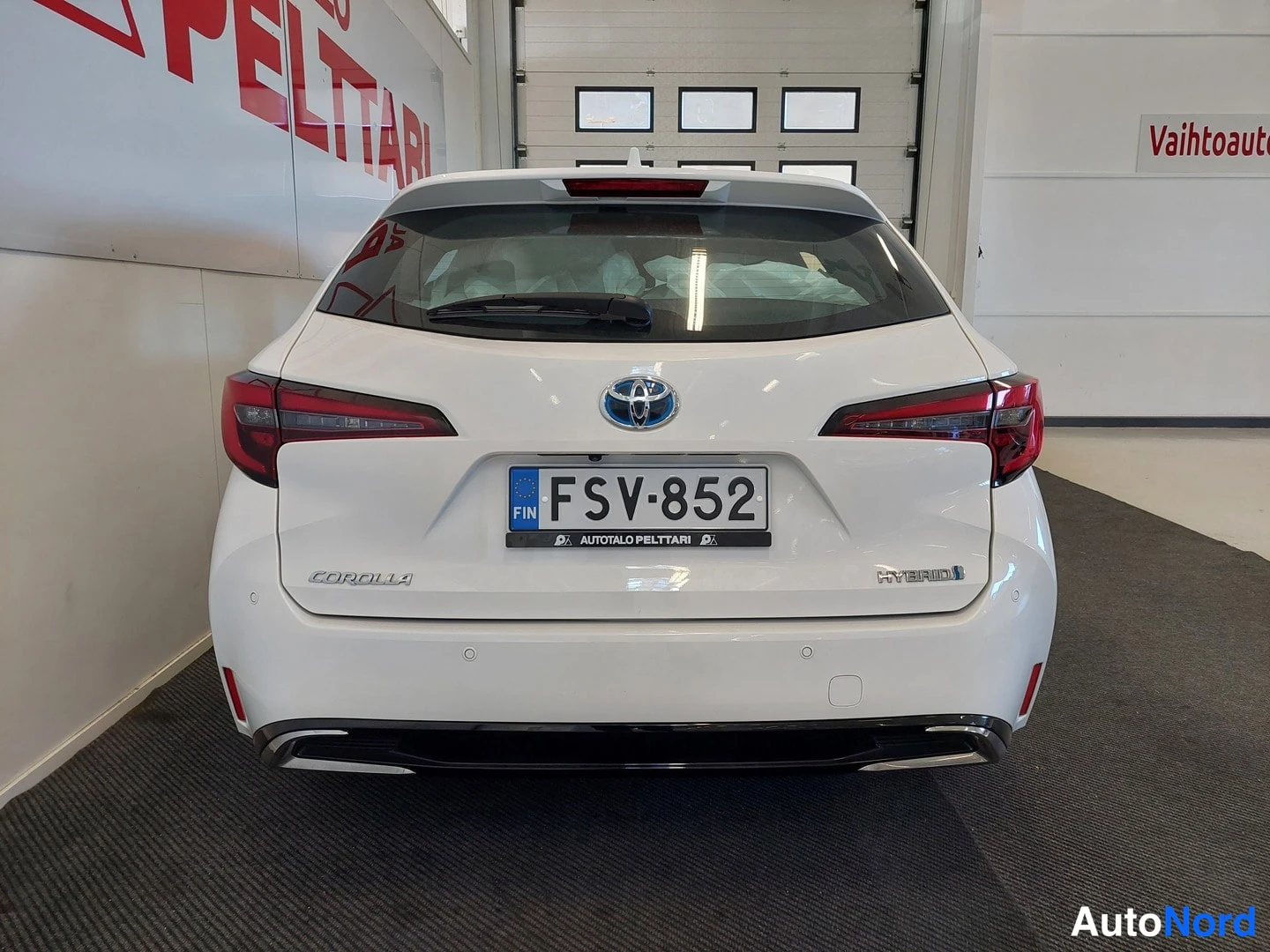 Takaa: Valkoisen Toyota Corollan takapää suoraan edestä, rekisterikilpi, HYBRID-merkintä ja Corolla-emblem näkyvät.