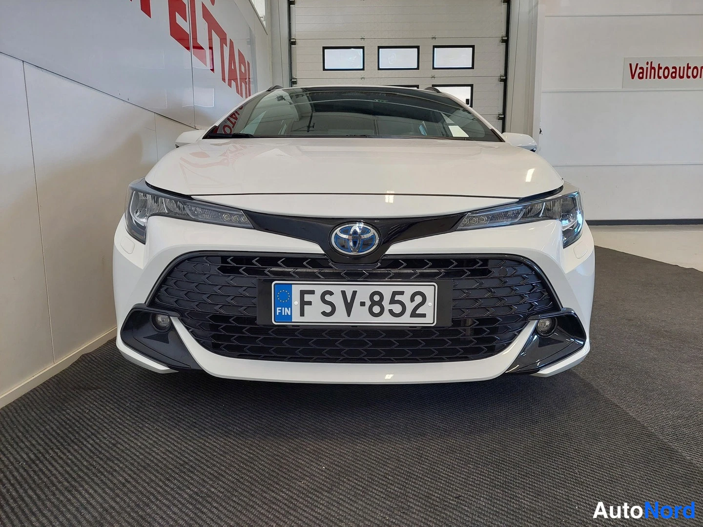 Edestä: Valkoisen Toyota Corollan etupää suoraan edestä, musta etusäleikkö ja rekisterikilpi.