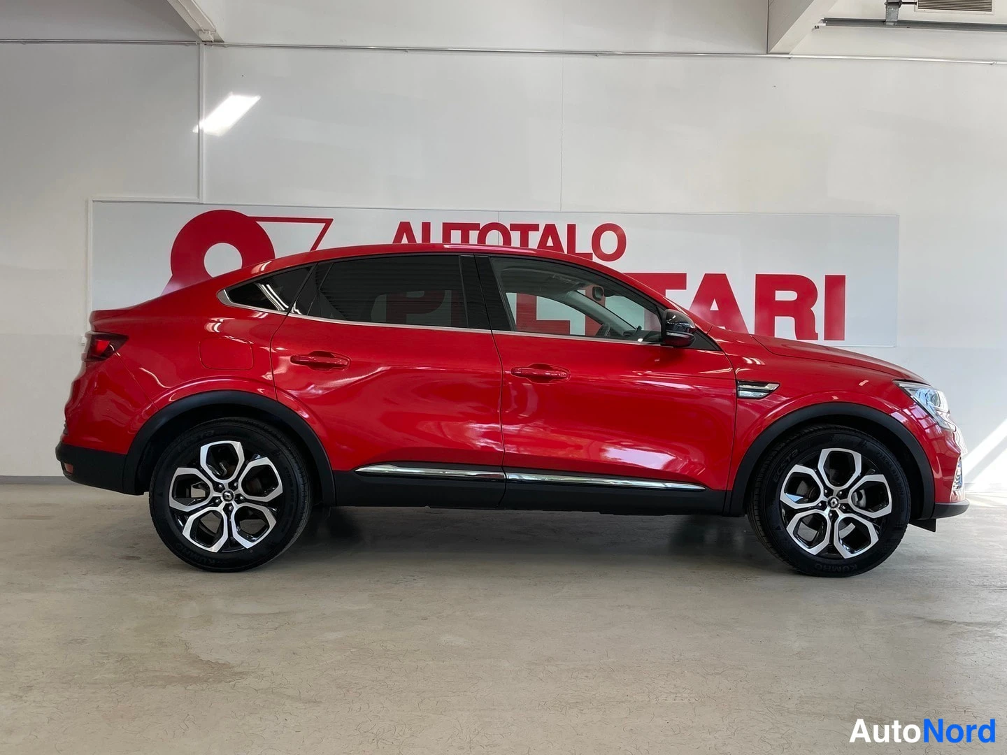 Sivulta: Punainen Renault Arkana -hybridimaasturin sivuprofiili myynnissä sisätiloissa.