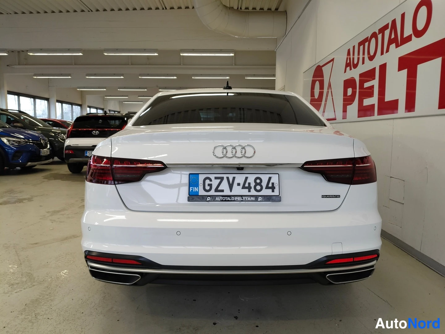 Takaa: Auton perä suoraan takaa valokuvausstudiossa; valkoinen sedan, Audi-merkki, takavalot ja rekisterikilpi.
