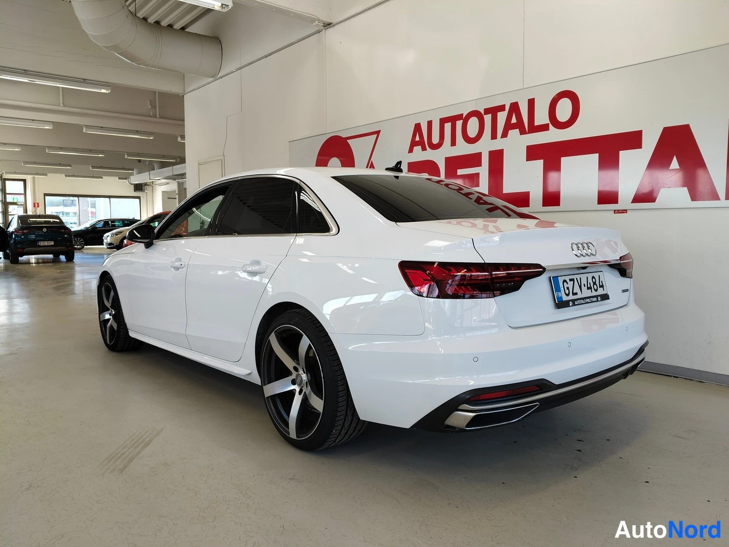 Takaviisto: Valkoinen Audi A4 -sedan tikkukulmasta takaa vasemmalta kuvattuna; punaiset takavalot, -rekisterikilpi ja tummat viisipuolaiset vanteet näkyvät.