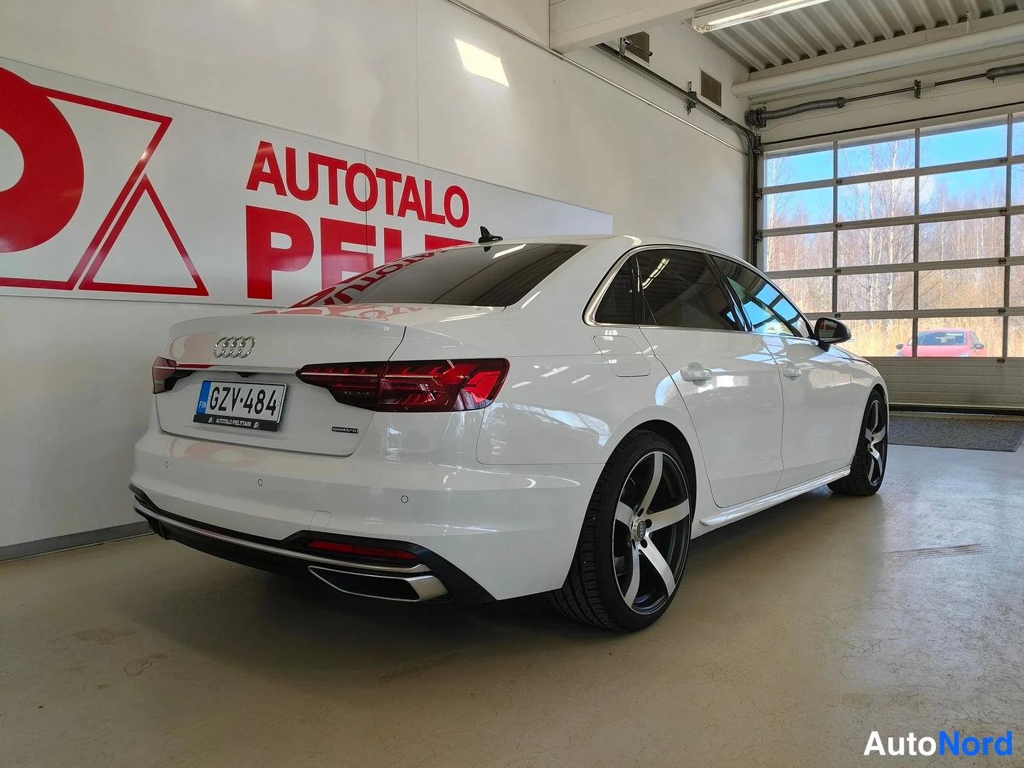 Takaviisto: Valkoinen Audi A4 -sedan tikkukulmasta takaa oikealta kuvattuna; punaiset takavalot, -rekisterikilpi ja tummat viisipuolaiset vanteet näkyvät.