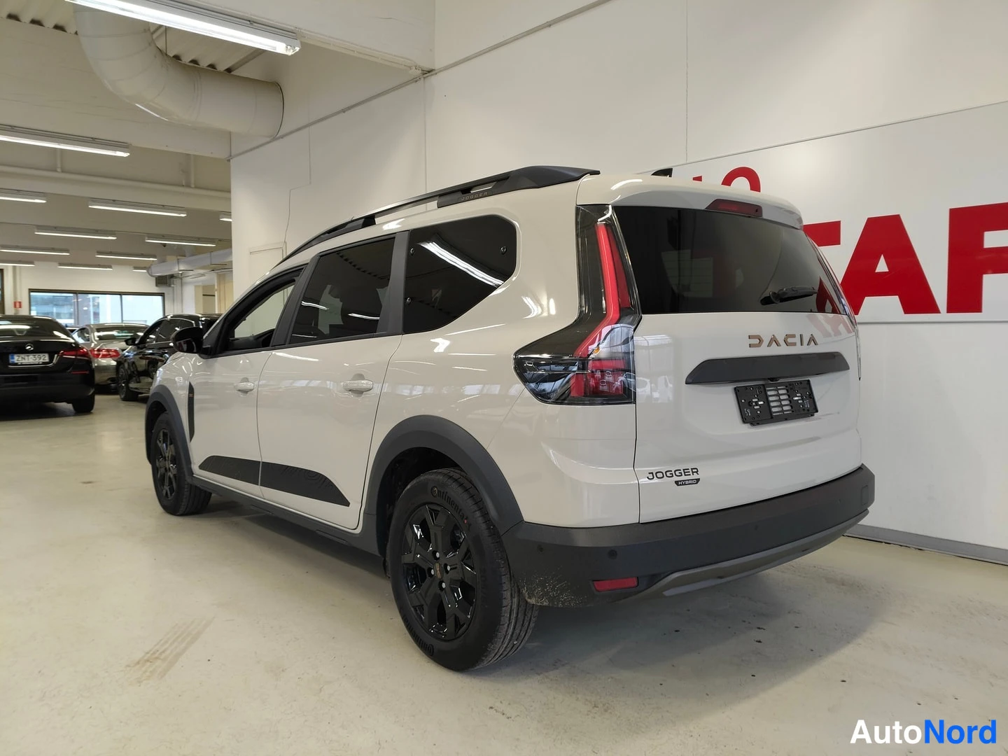 Takaviisto: Takakulmasta kuvattu valkoinen Dacia Jogger -tila-auto, jossa tummat kevytmetallivanteet ja kattokaiteet.