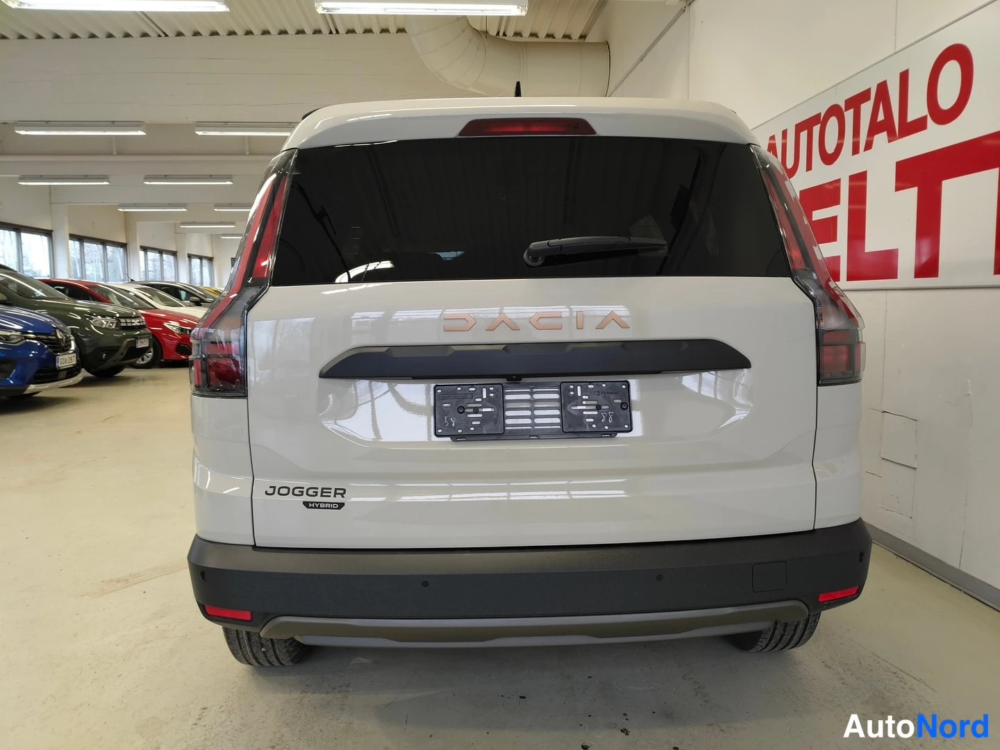 Takaa: Auton takaosa suoraan takaa: DACIA-merkintä ja JOGGER Hybrid -teksti, tummat takavalot ja tyhjä rekisteripaikka.