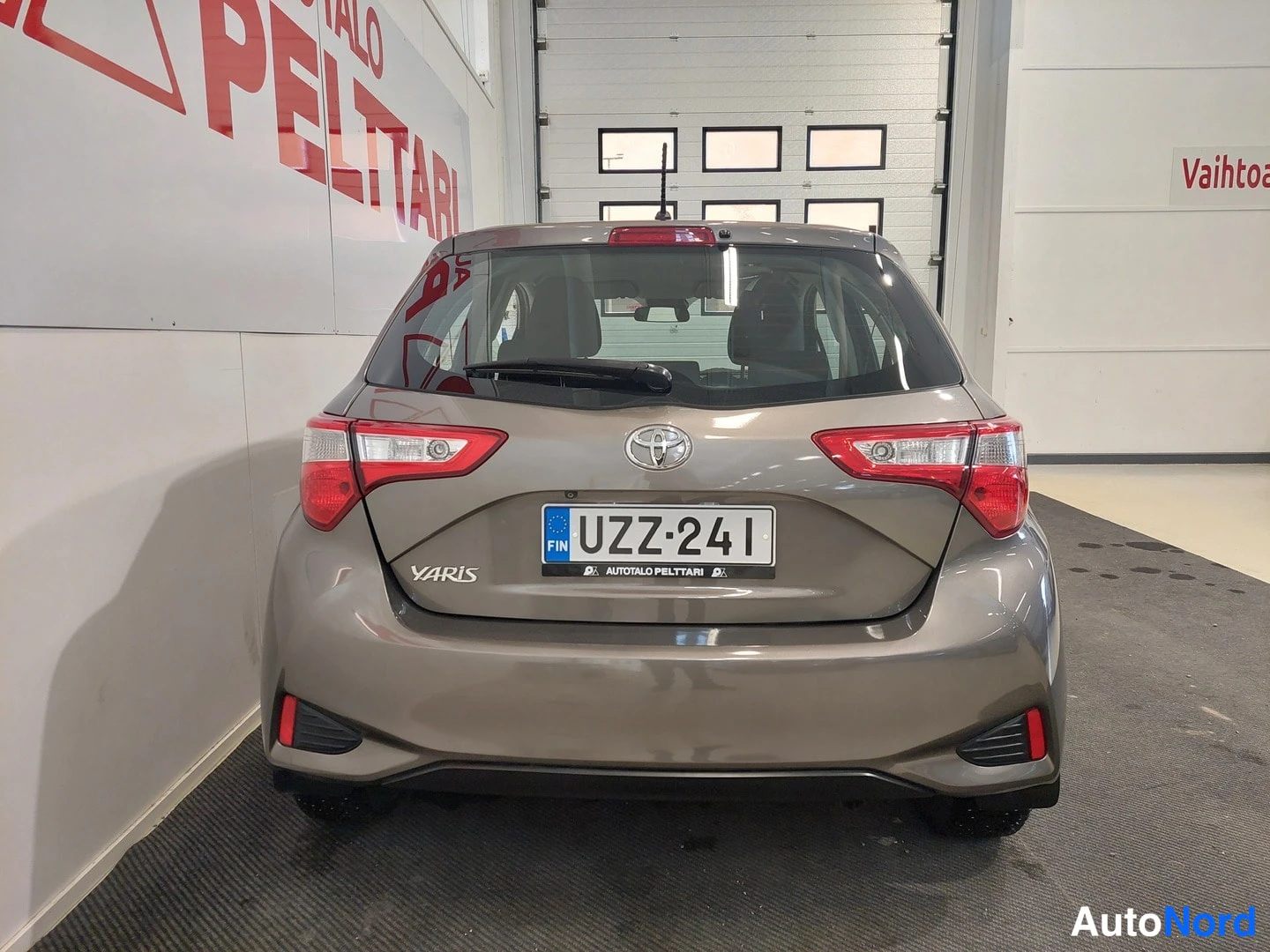 Takaa: Auton takaosa suoraan takaa; ruskeaharmaa hatchback, Toyota-merkki, YARIS-teksti ja rekisteritunnus.