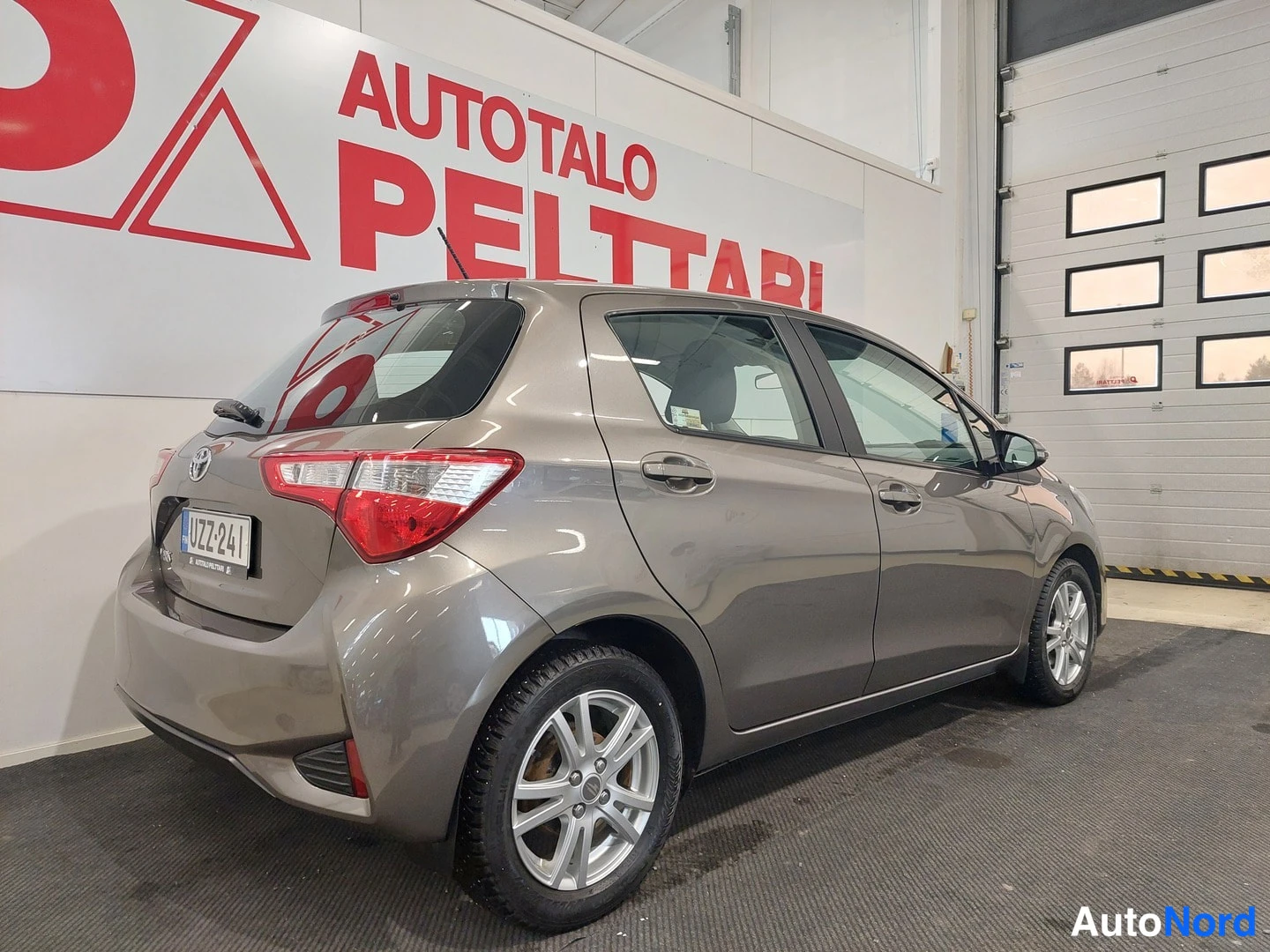Takaviisto: Ruskeanharmaan Toyota Yaris -henkilöauton takakulma näkyy sisätiloissa, rekisterikilpi.