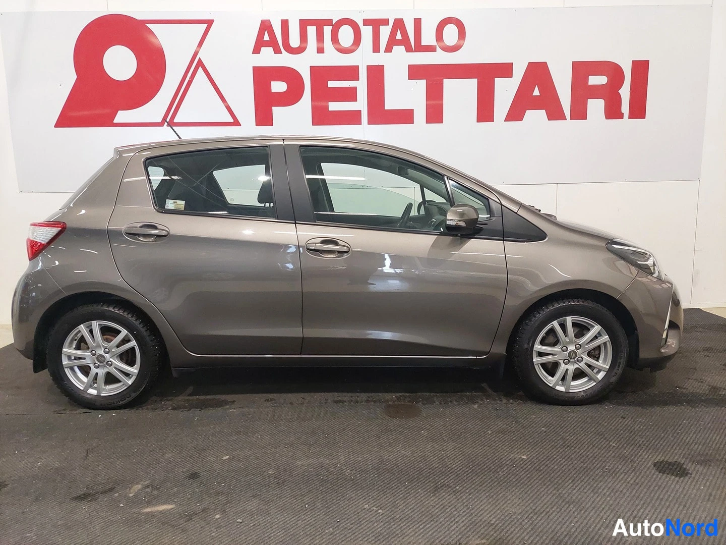 Sivulta: Sivukuva ruskeanharmaasta Toyota Yaris -henkilöautosta autonäyttämöllä.