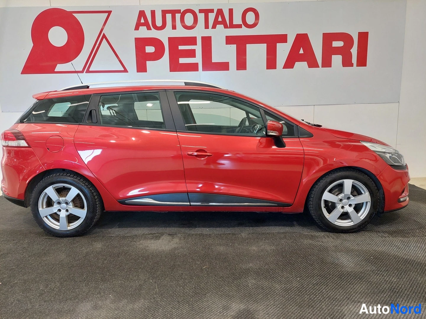 Etuviisto, nokka oikealle: Punaisen Renault Clio -farmarin etuosasta oikealle kuvattu sivunäkymä, hopeavanteet ja kattokaiteet näkyvät.