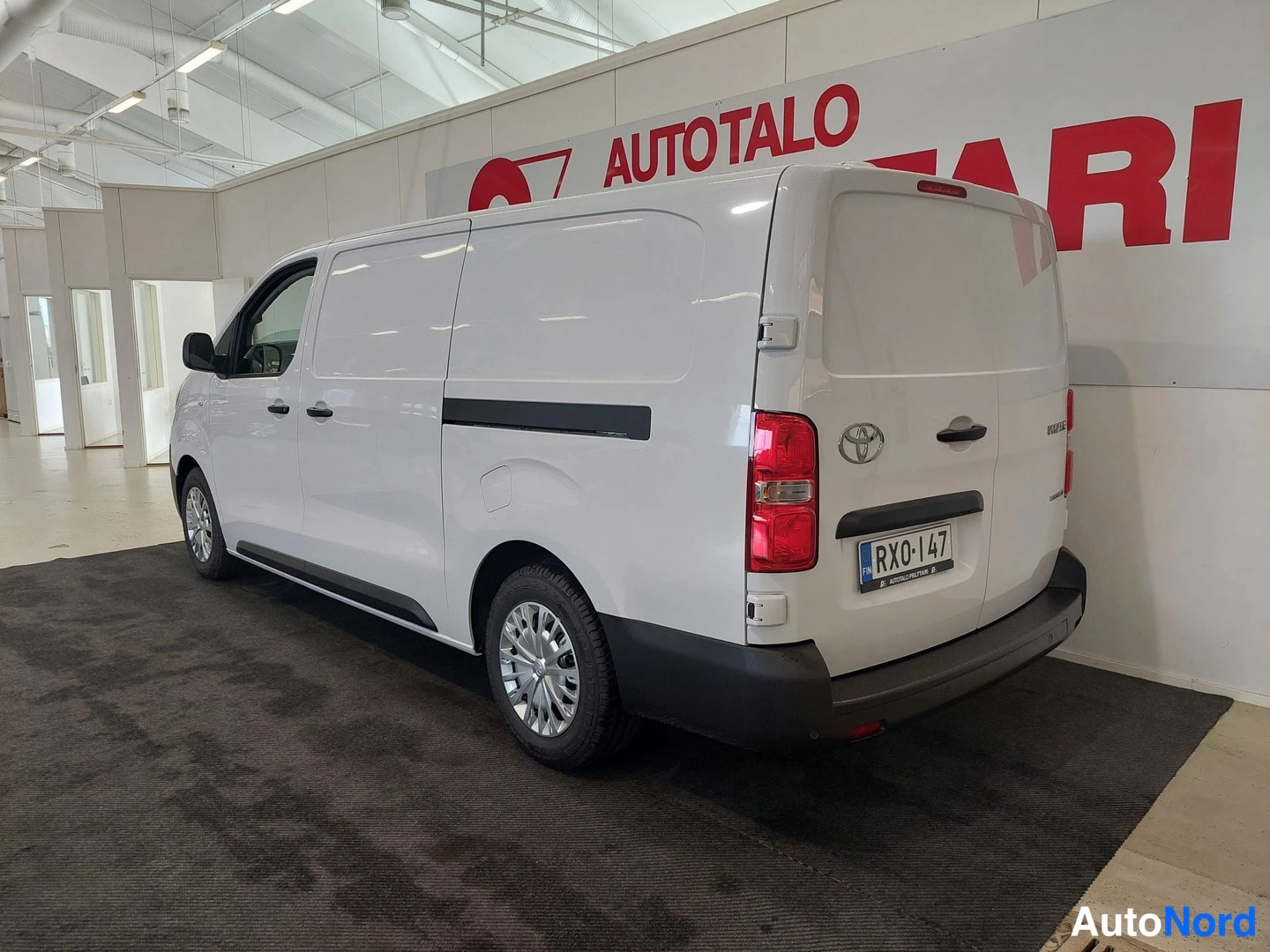 Takaviisto: Valkoinen Toyota Proace -pakettiauto taka kolmannes kuvakulmasta showroomissa