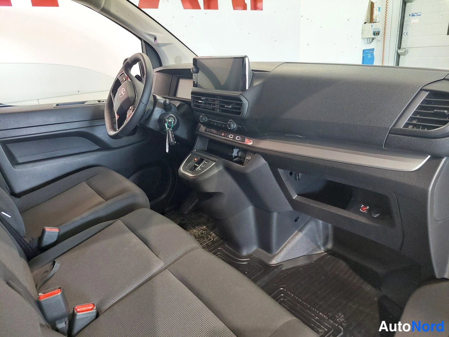 Muu: Auton sisätilat: tumma ohjaamo, Toyota-ohjauspyörä, kojelaudalla näyttö, kaksipaikkainen penkki etumatkustajan puolella ja tummat matot lattiassa.