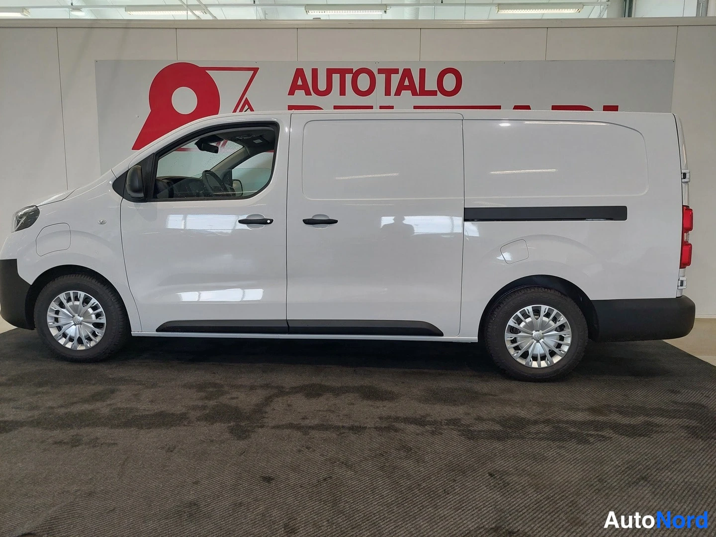 Sivulta: Valkoinen Toyota Proace -pakettiauto sivulta showroomissa