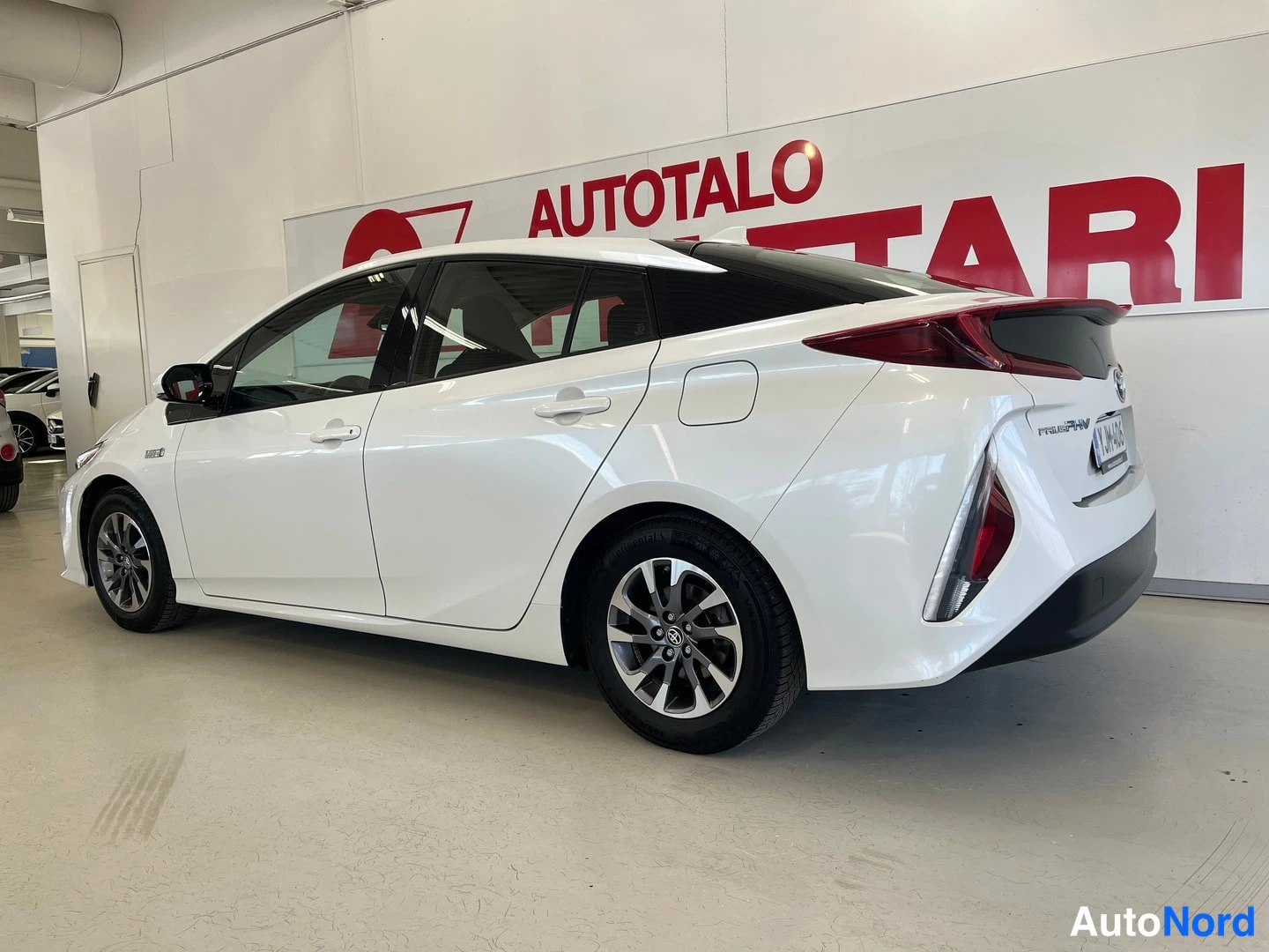 Takaviisto: Valkoinen Toyota Prius Plug-In -henkilöauto kuvattu kolmannelta takanäkymältä sisätiloissa, perän ja vasemman sivun ollessa näkyvissä.