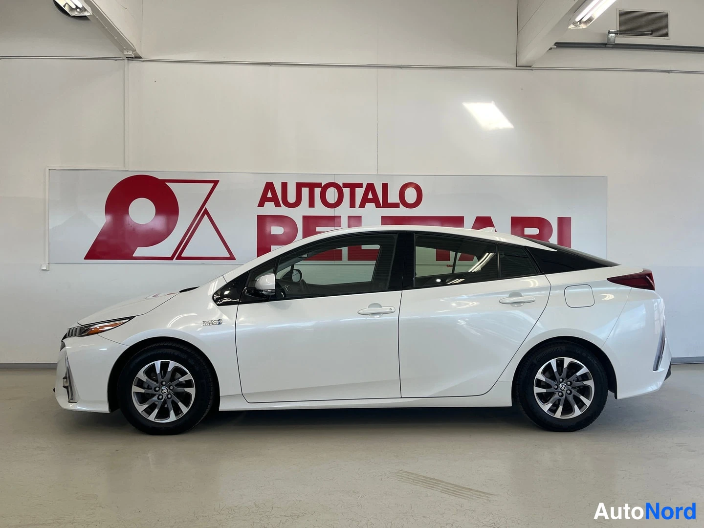 Sivulta: Valkoinen Toyota Prius Plug-In -henkilöauto sivulta kuvattuna sisätiloissa.