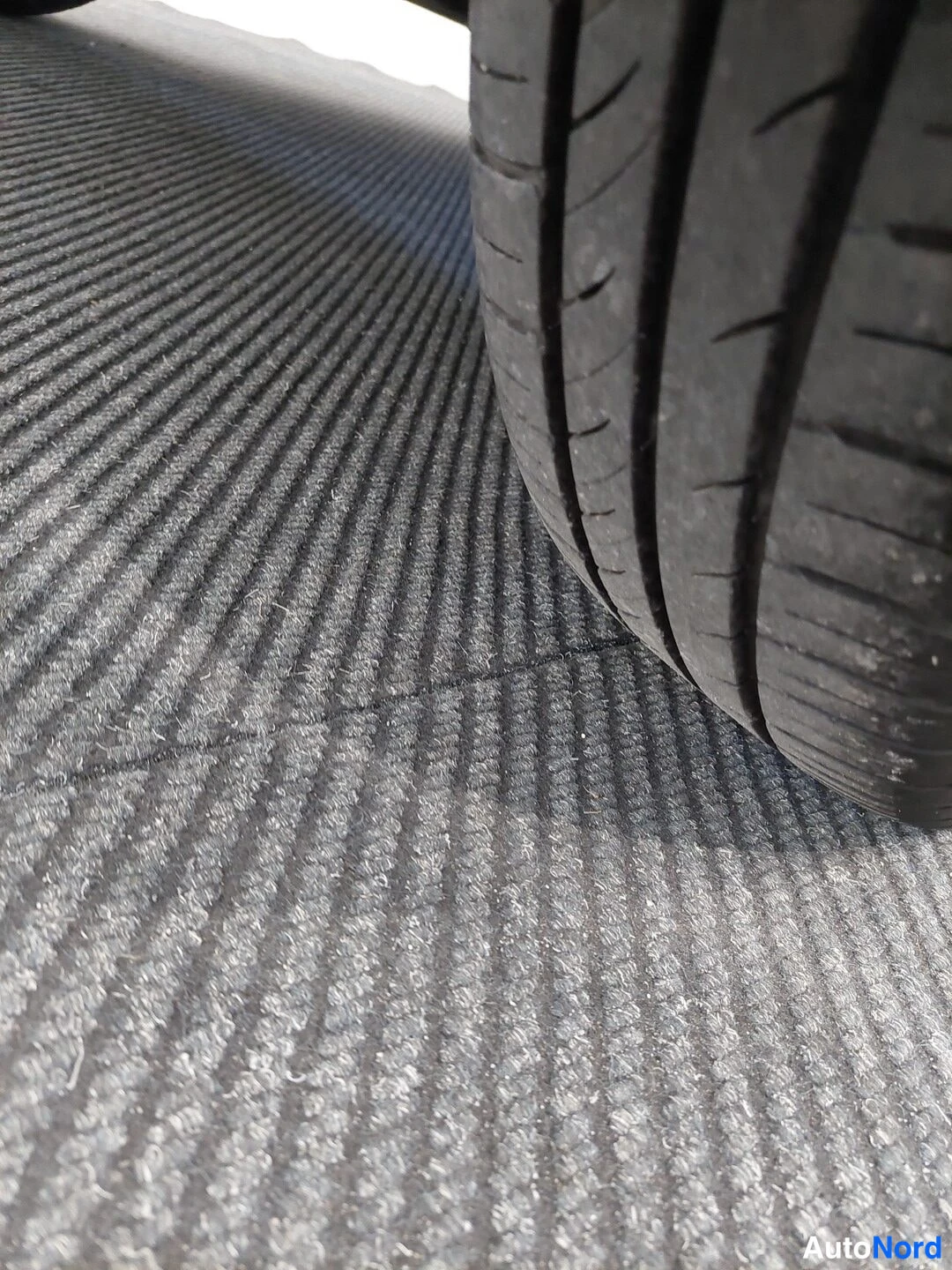 Muu: Lähikuva auton renkaasta ja kuivattulta harmaalta parkkimatolta.