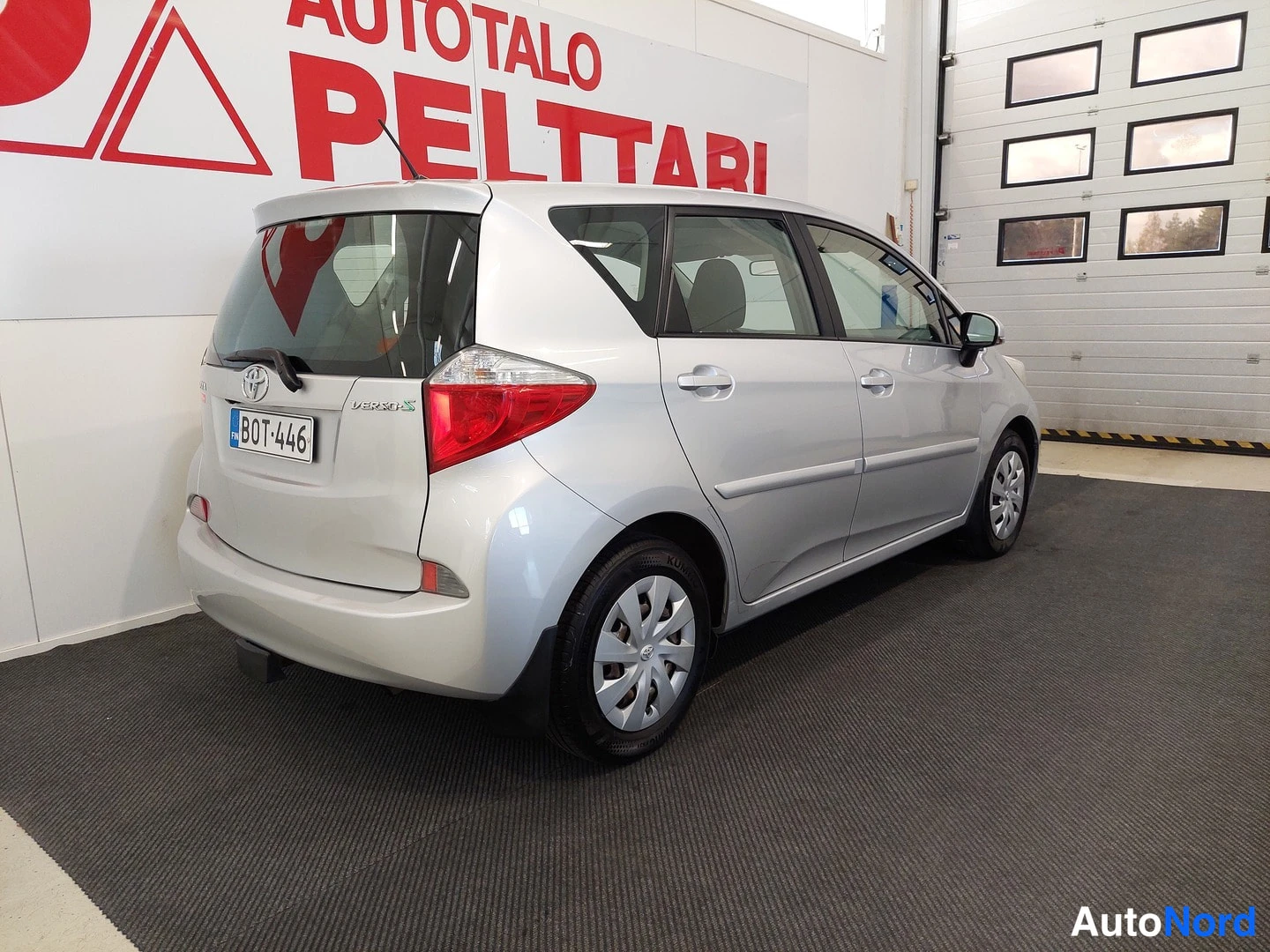 Takaviisto: Hopeanharmaan Toyota Verso-S:n takaosa ja oikea kylki näkyvät Autoatalo Peltarin tiloissa; takaluukissa Toyota-merkki ja VERSO-S-tunnus, rekisterikilpi.