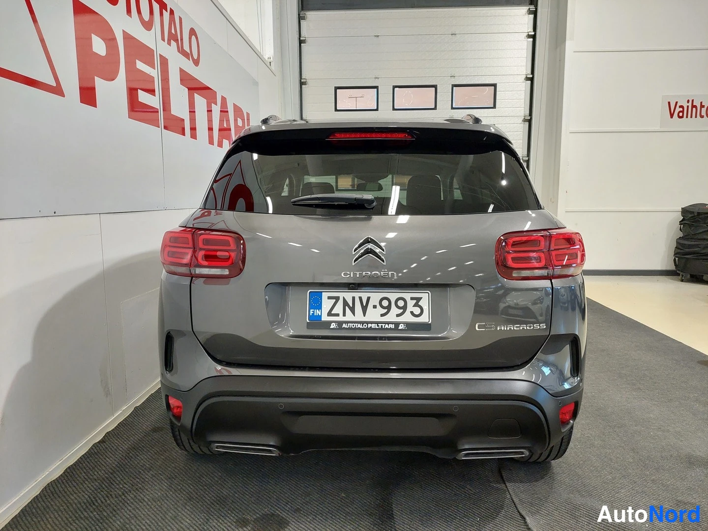 Takaa: Auton takaosa suoraan takaa: tummanharmaa Citroën C5 Aircross, rekisteritunnus, kattokaiteet näkyvät sisätiloissa.