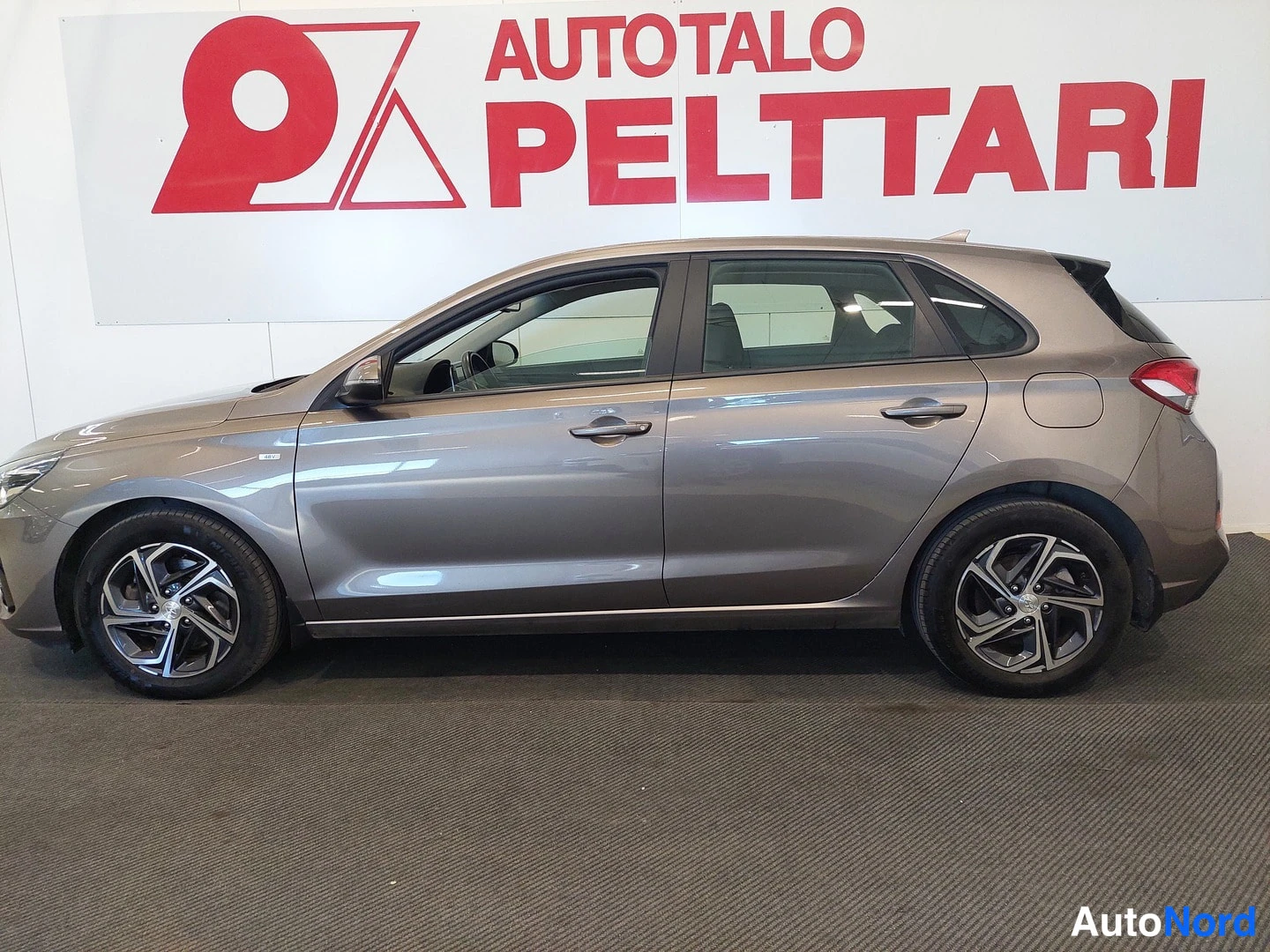 Sivulta: Hyundai i30 -vaunuporras... tauko. Sivukuva ruskeanharmaasta viistoperäisestä Hyundai i30 -henkilöautosta sisätiloissa, kylki ja renkaat näkyvät.