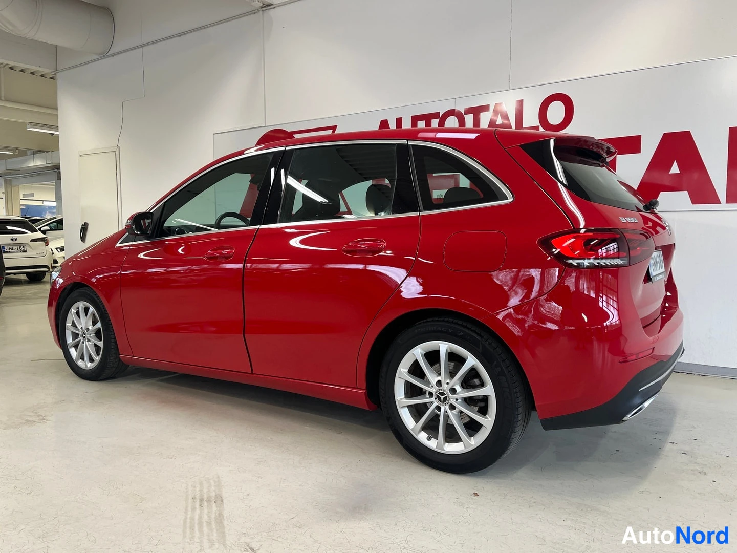 Takaviisto: Punaisen Mercedes-Benz B-sarjan auton takakulma ja kylki oikealta kuvatussa sisätilakuvassa.