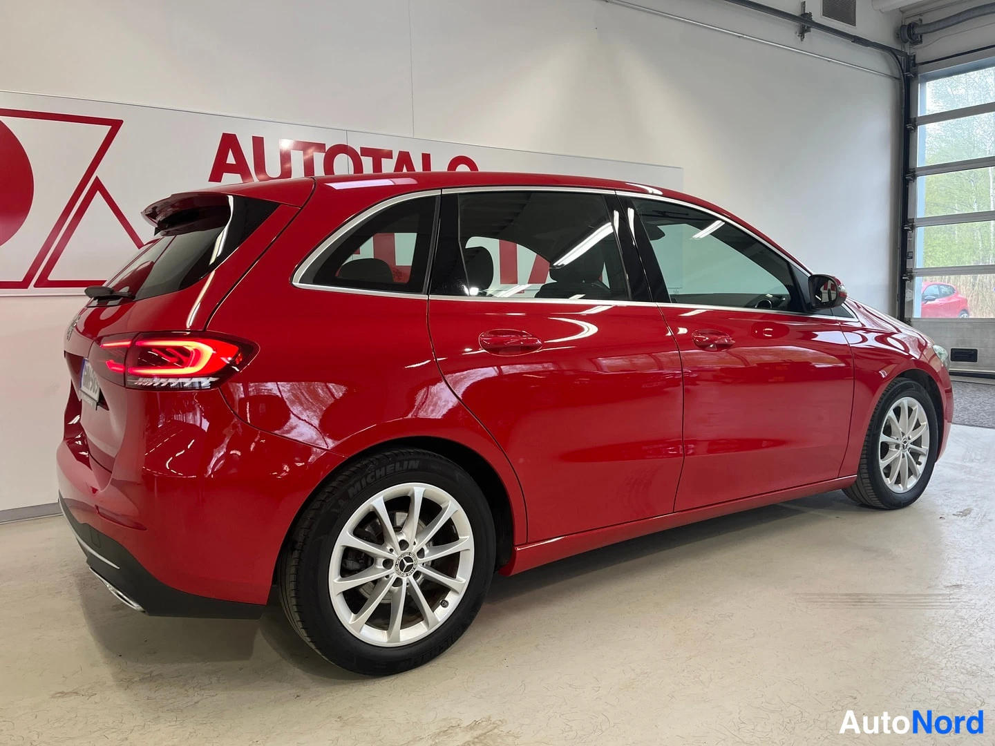 Takaviisto: Punaisen Mercedes-Benz B-sarjan auton takakulma ja kylki vasemmalta kuvatussa sisätilakuvassa.