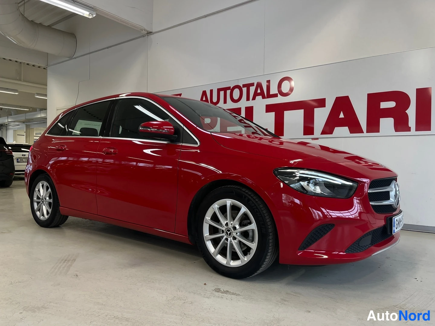 Etuviisto, nokka oikealle: Punainen Mercedes-Benz B-luokan farmarimallinen tila-auto kuvattu kolmeneljänneskulmasta etupää oikealla hallissa, valkoisella Autotalo Pelttari -taustas