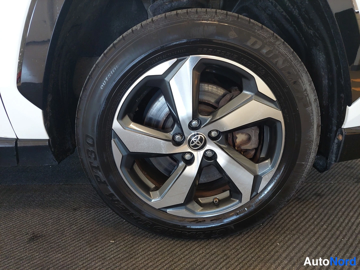 Yksityiskohta: Ajovalo Toyota-kevytmetallivanne ja Dunlop-kesärengas lähikuvassa, jarrulevy näkyvissä.