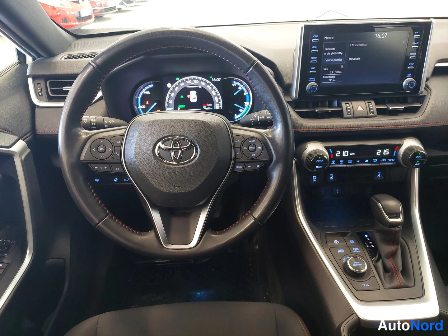 Muu: Ohjaamo näytöltä: Toyota-ohjauspyörä, hybridimittaristo, keskellä kosketusnäyttö ja automaattivaihteen valitsin.