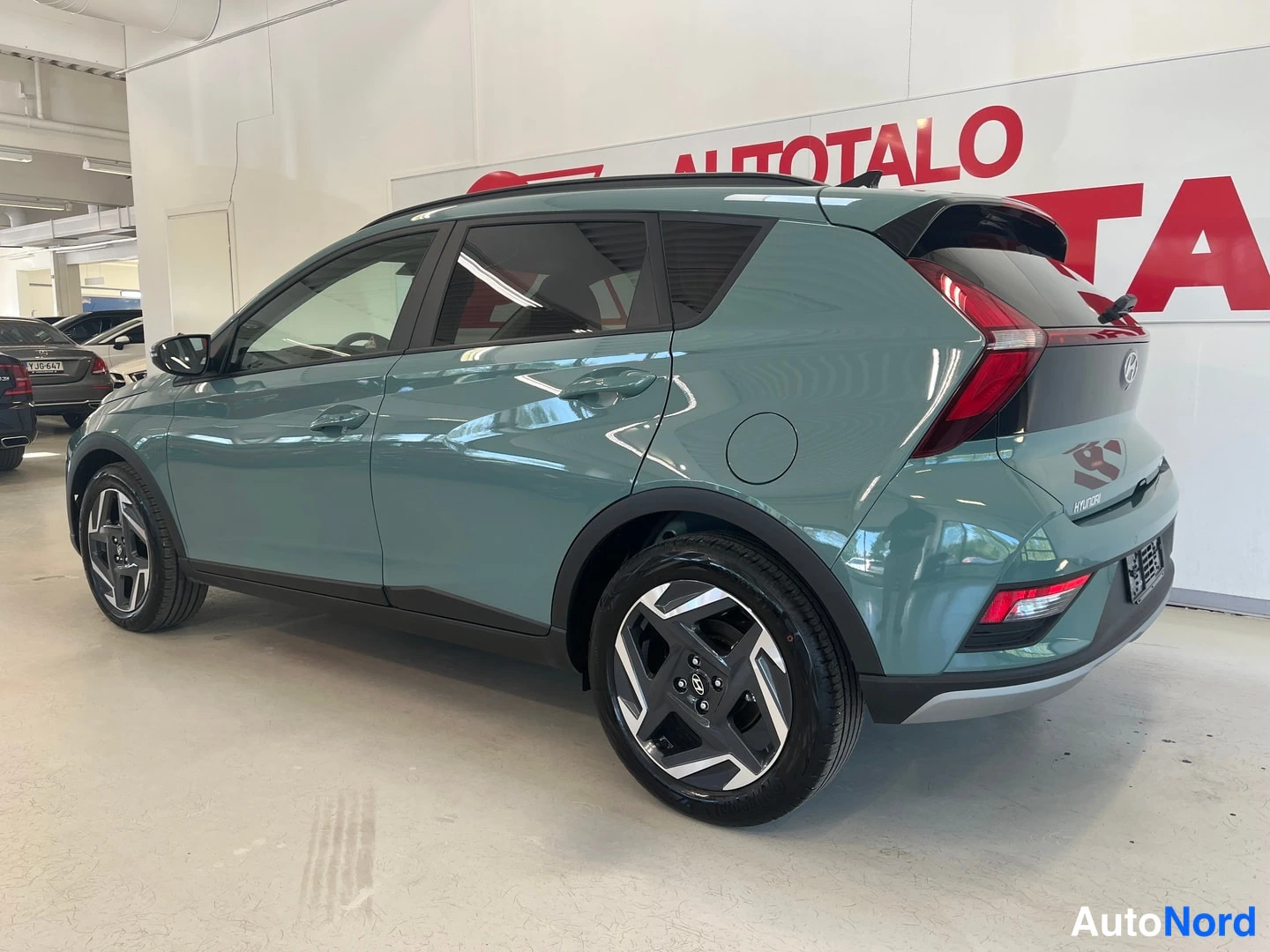 Takaviisto: Hyundai Bayon -kompakti-SUV harmaanvihreällä korilla kuvattu takaosa ja vasen sivu sisätiloissa.