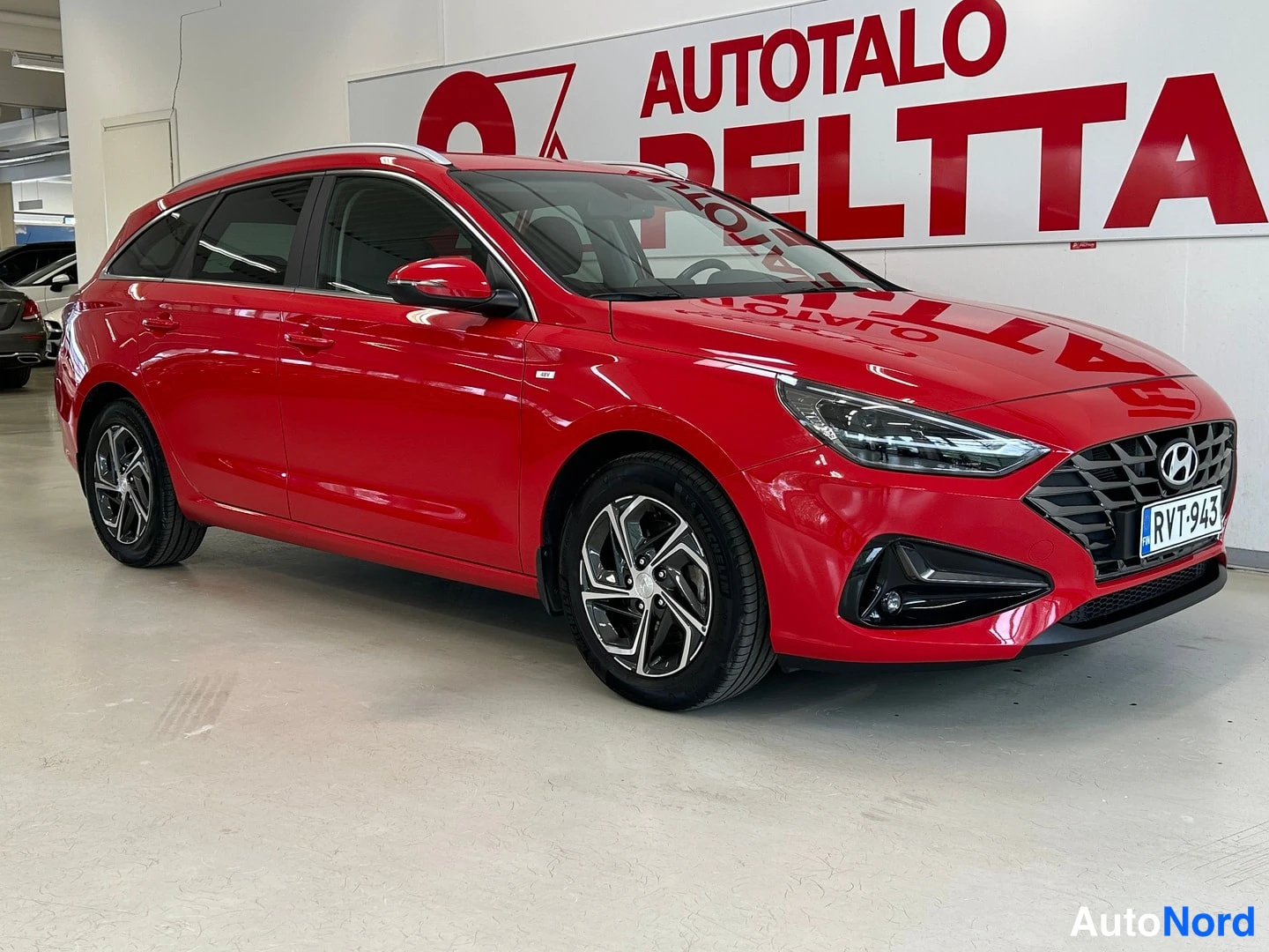 Etuviisto, nokka oikealle: Punaisen Hyundai i30 Farmi -auton etukulma sisätiloissa, rekisterikilpi etualalla.