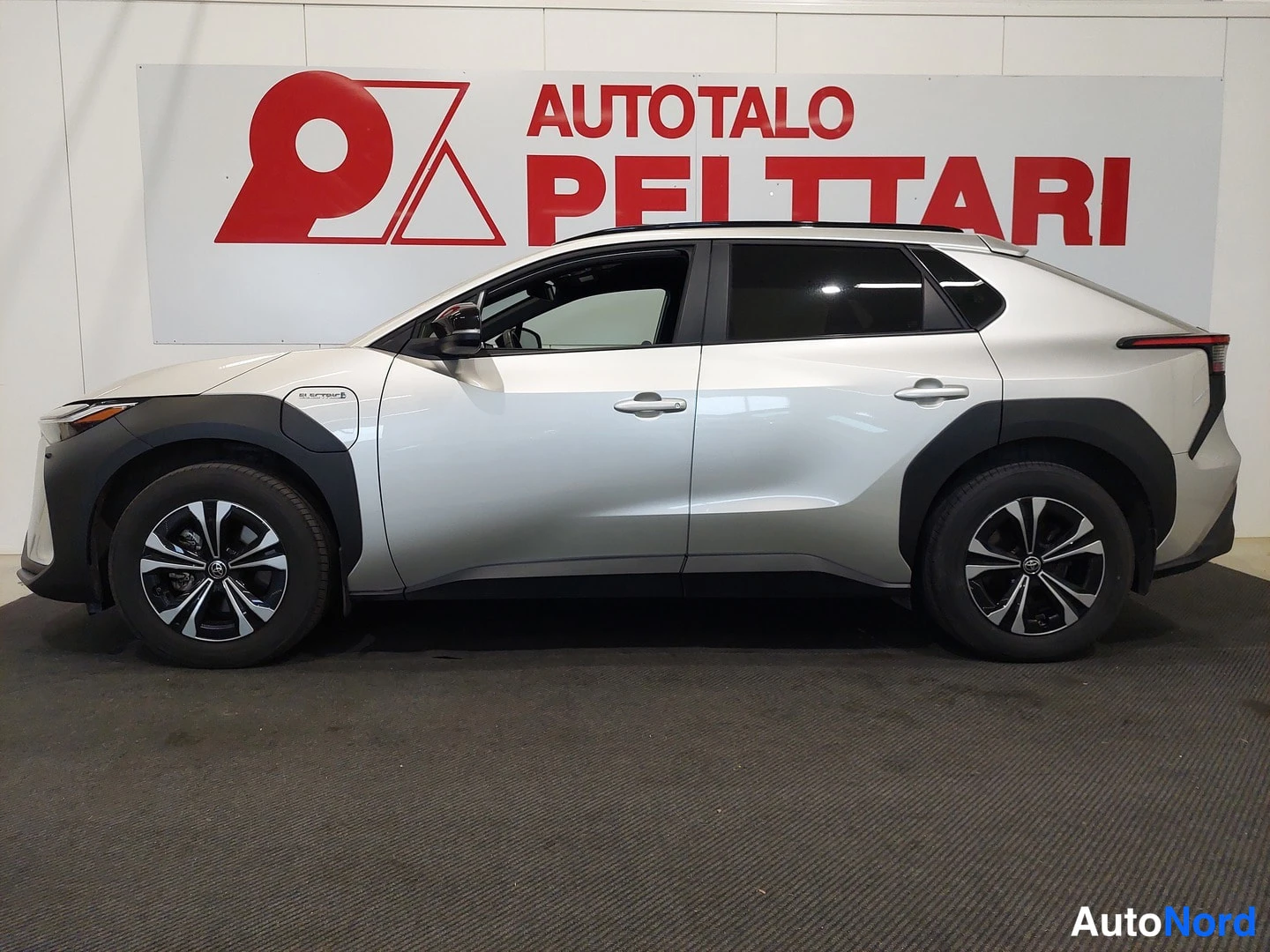Etuviisto, nokka vasemmalle: Hopeanvärisen Toyota bZ4X:n sivuprofiili oikealta puolelta sisätiloissa.
