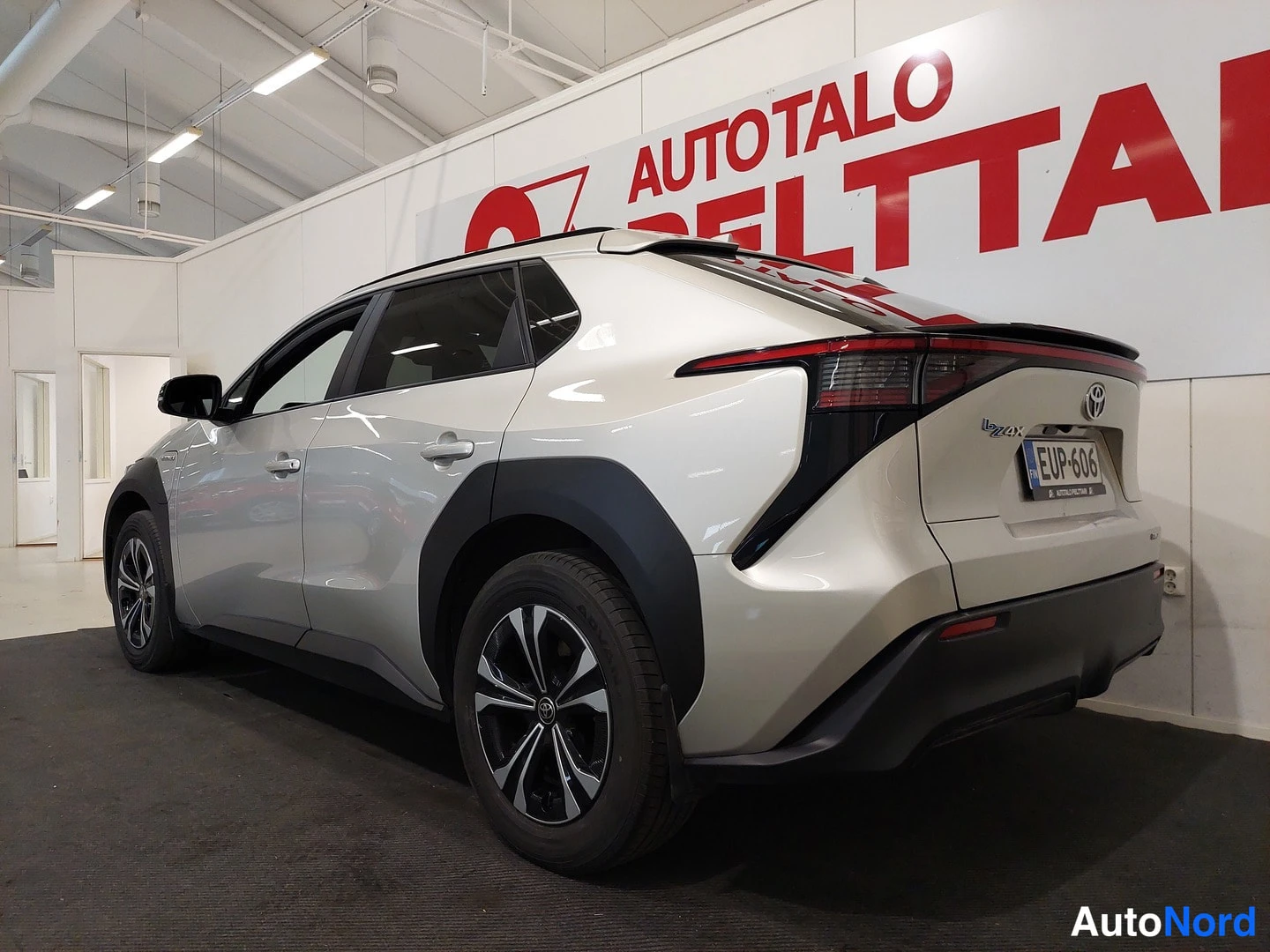 Takaviisto: Hopeanvärisen Toyota bZ4X:n takanurkka kolmivälikulmassa sisätiloissa, rekisteritunnus.
