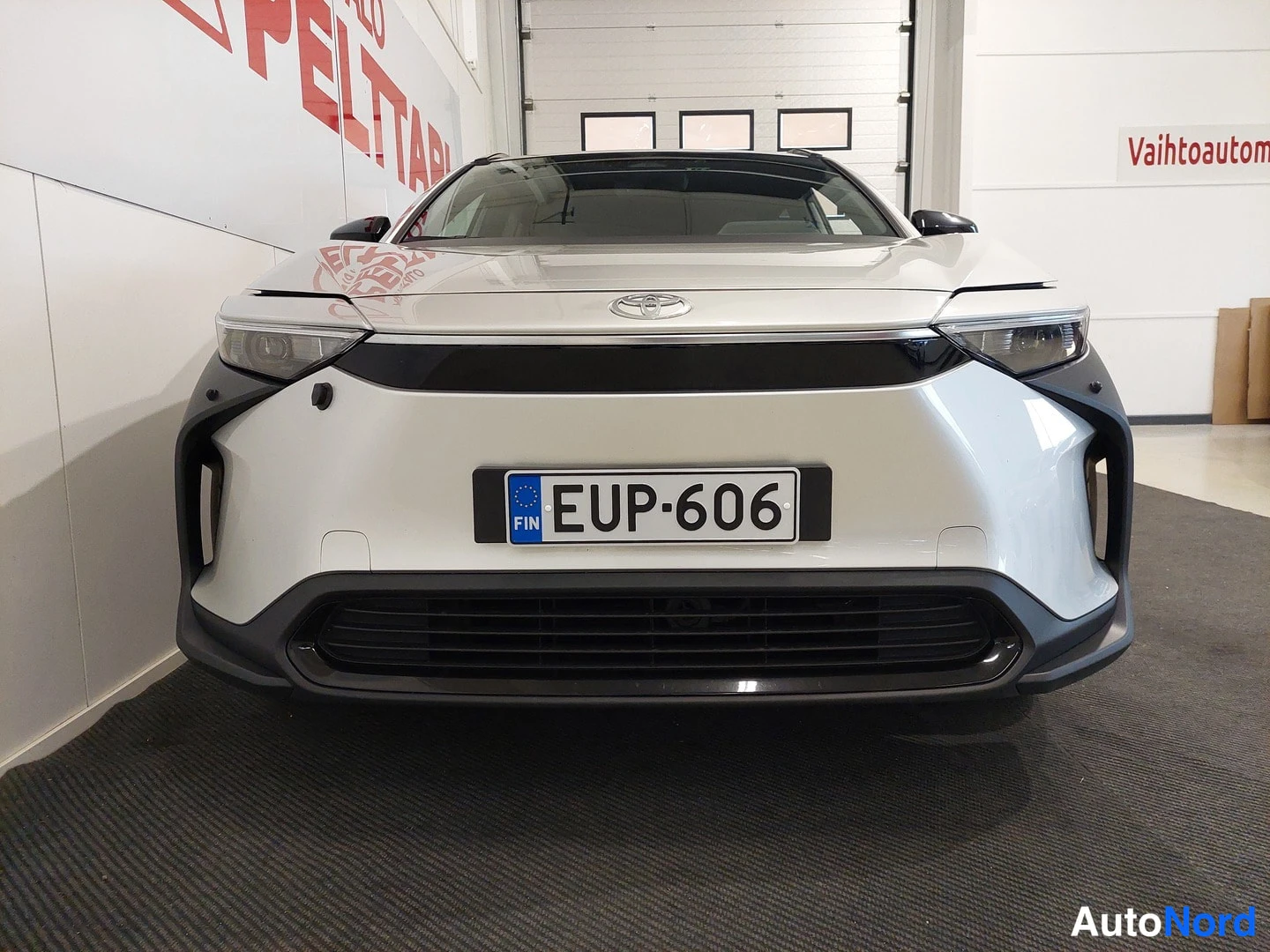 Edestä: Valkoisen Toyota bZ4X:n etunäkymä hallissa, rekisterikilpi.