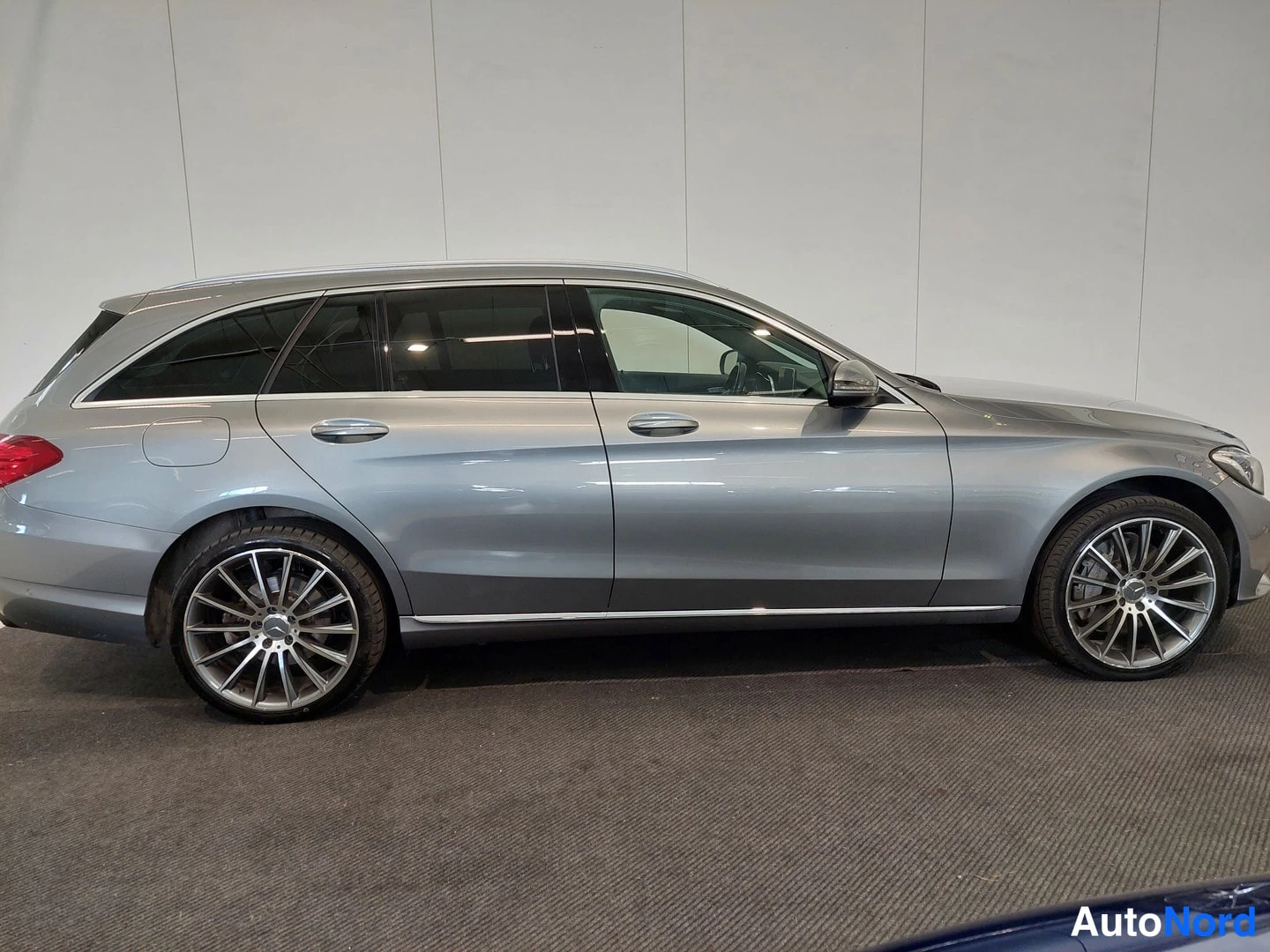 Sivulta: Hopeanharmaan Mercedes-Benz farmariauton sivuprofiili sisätiloissa, kevytmetallivanteet ja tummat ikkunat.