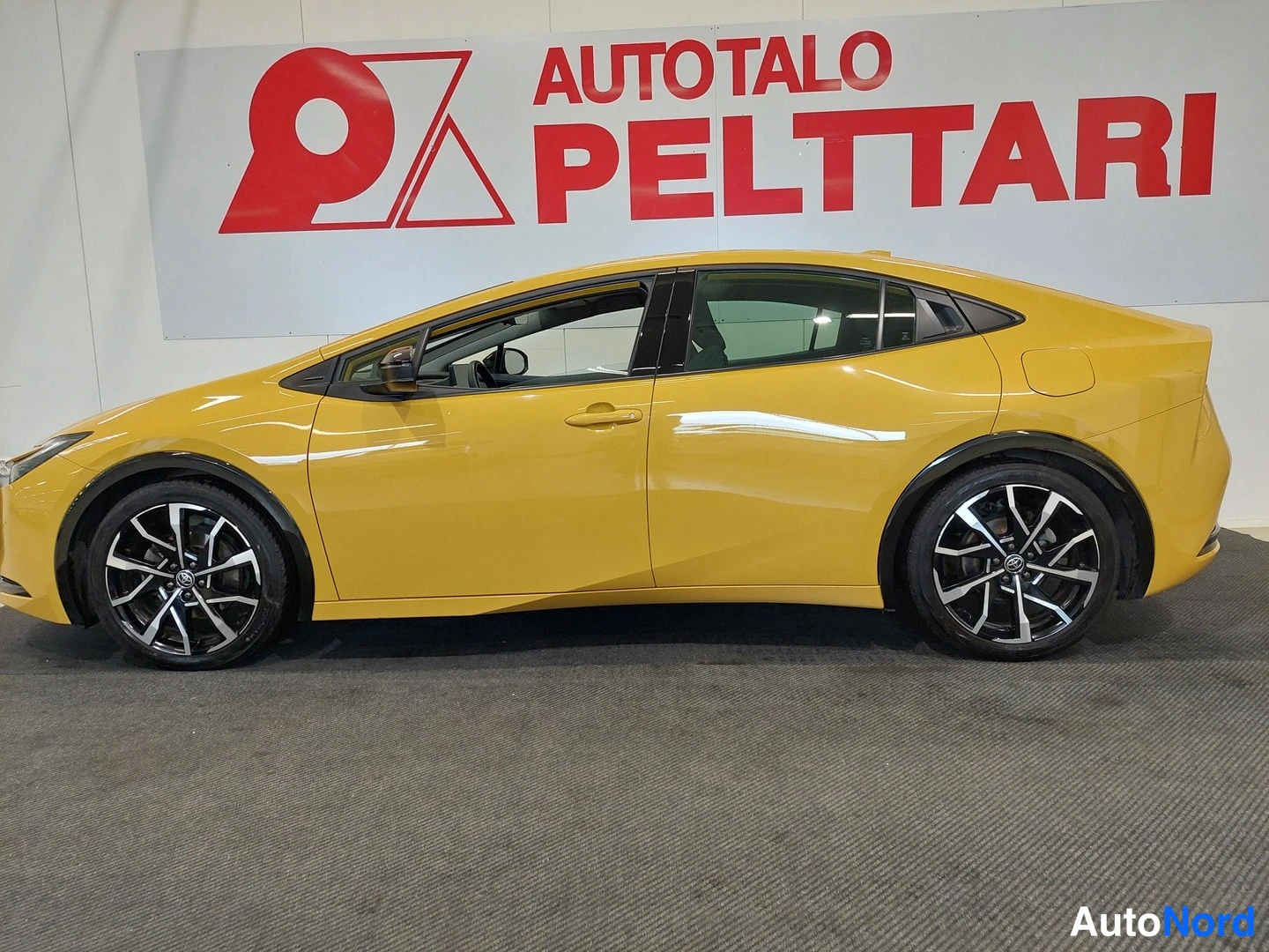 Sivulta: Keltaisen Toyota Prius -henkilöauton kylki sivusuunnasta sisätiloissa.