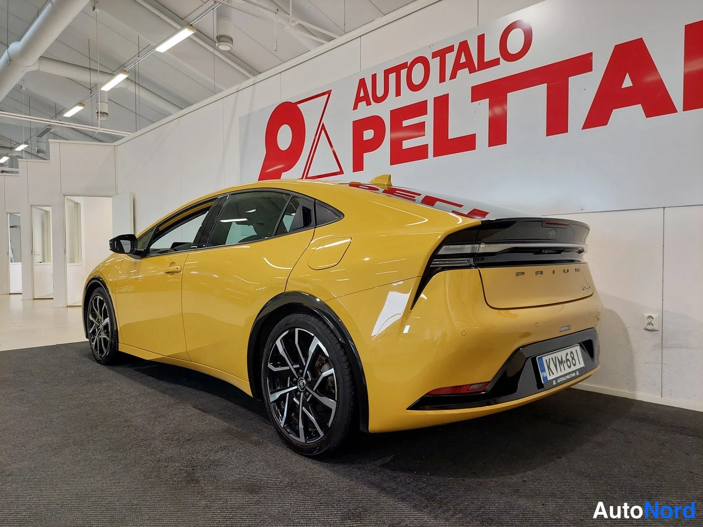 Takaviisto: Keltaisen Toyota Prius -auton takaosa ja kylki takaviistosta oikealta nähtynä, rekisterikilpi.