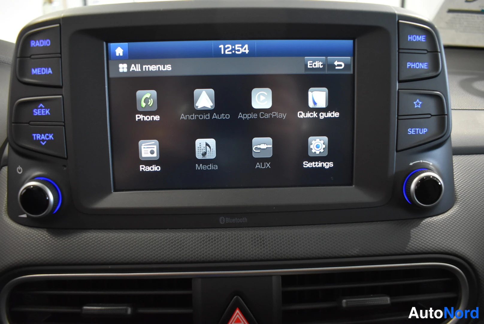 Muu: Auton kojelaudan kosketusnäyttö, jossa näkyvät valikot Phone, Android Auto, Apple CarPlay, Quick guide, Radio, Media, AUX ja Settings, kellonaikana 12:54.