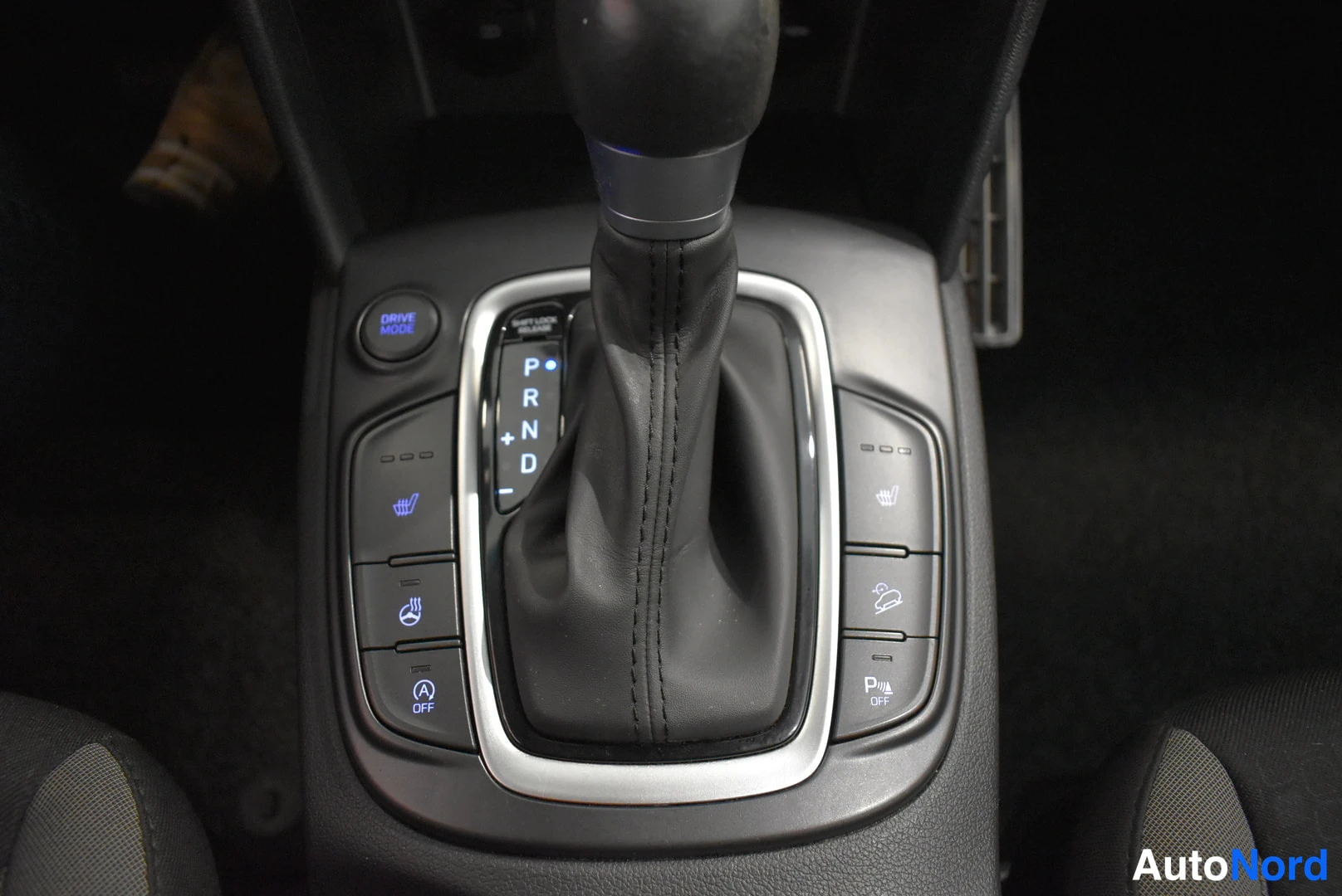 Edestä: Automaattivaihteiston valitsin asemissa P, R, N ja D sekä keskikonsolin painikkeet, muun muassa Drive Mode ja kiinteistöjänneDigiturvalaitteiden symbolit.