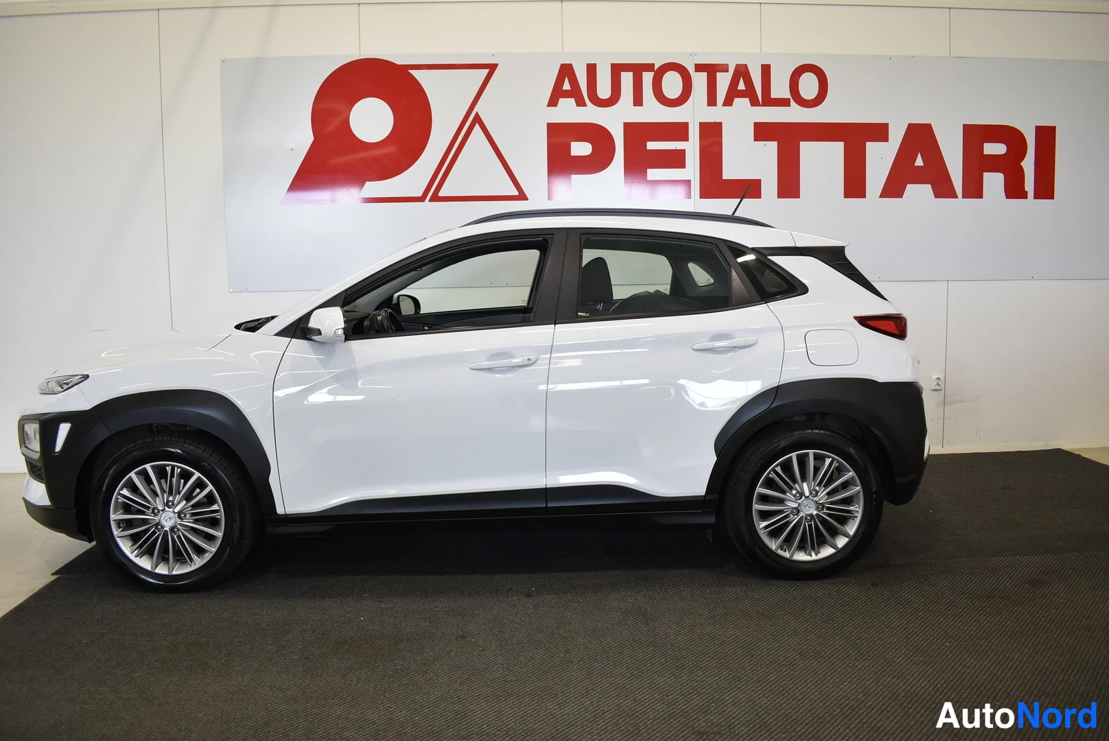 Etuviisto, nokka vasemmalle: Hyundai Kona -porsskatvekuva, valkoinen korimaalari, katukuva sivulta.