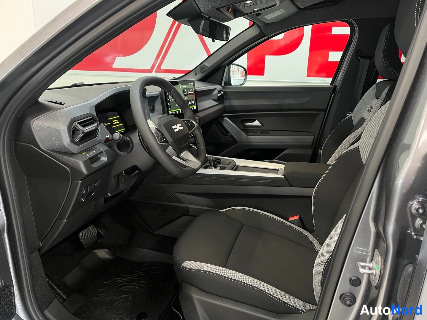 Muu: Dacia Bigsterin ohjaamo kuljettajan puolelta: ohjauspyörä, infotainment-näytöt ja etuistuin näkyvät.