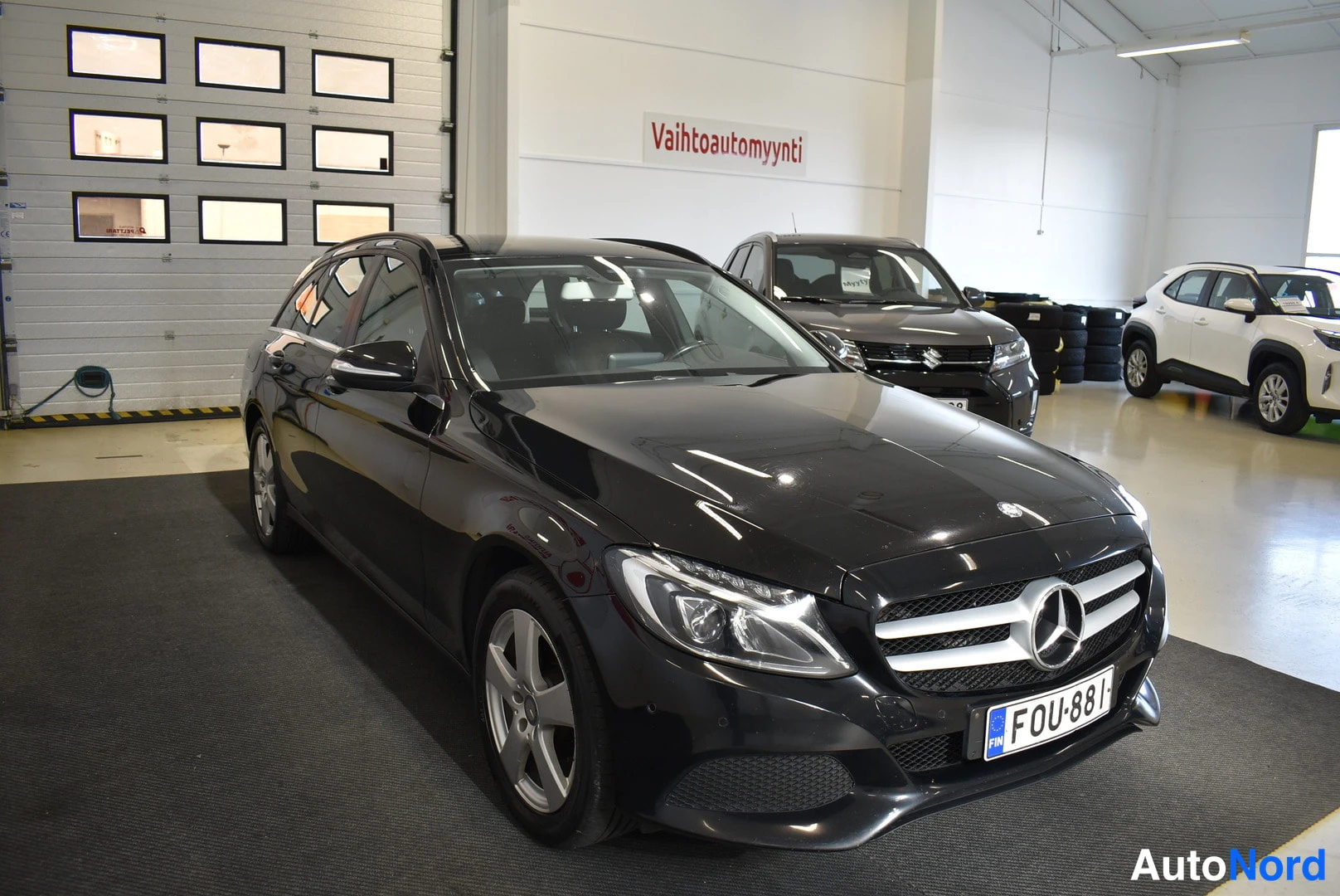 Etuviisto, nokka oikealle: Musta Mercedes-Benz farmari sivulta-etukulmasta osoittaen oikealle; rekisterikilpi.