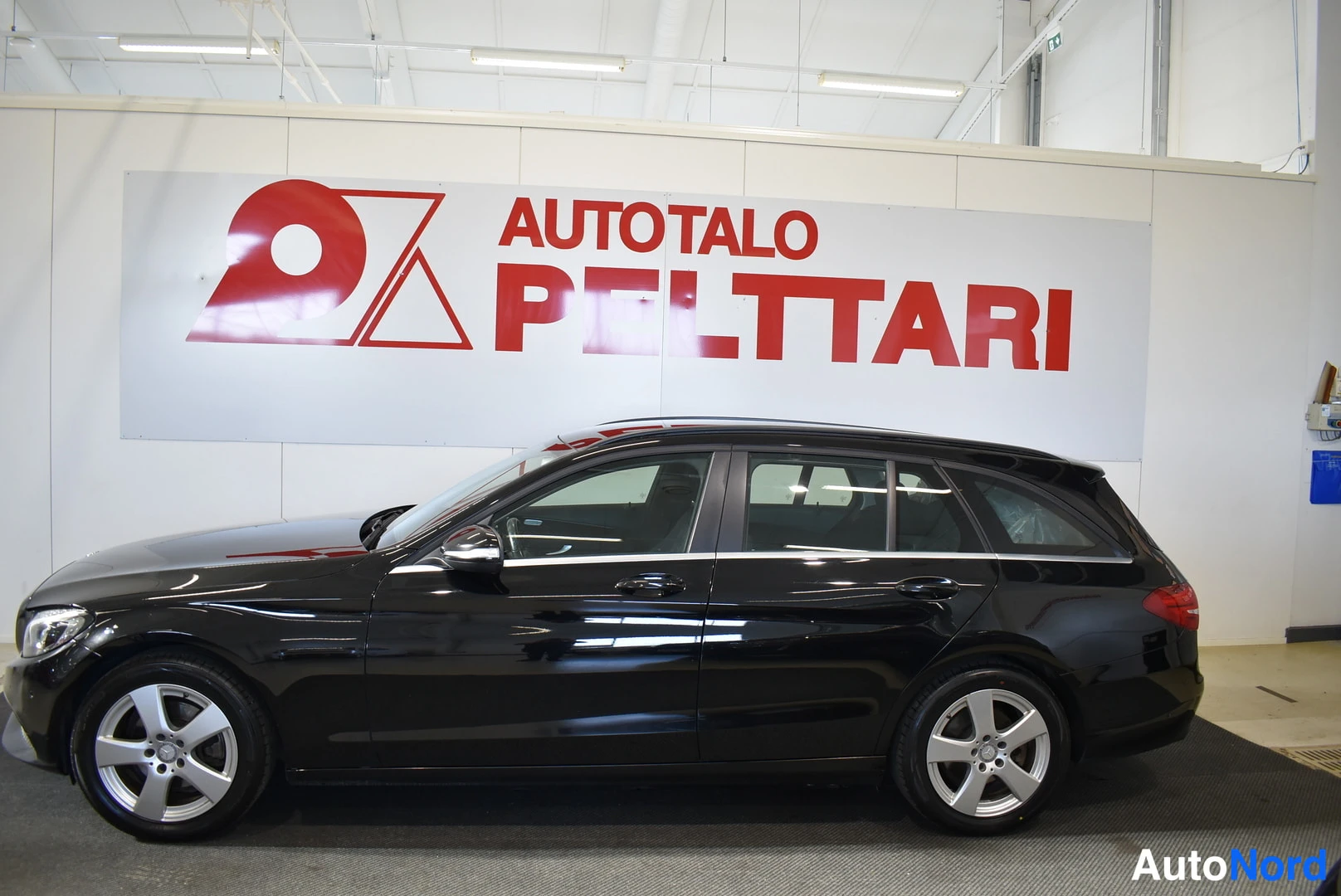 Sivulta: Mustan Mercedes-Benz farmarin sivuprofiili vasemmalta; viisiovinen kori ja hopeavanteet erottuvat.