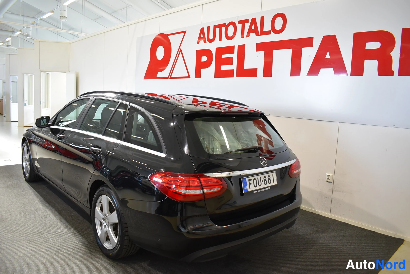 Takaviisto: Musta Mercedes-Benz -farmari kuvattu takaa-vinosti sisätiloissa; rekisterikilpi lukee ja takana näkyy Mercedes-tähti ja punaiset takavalot.