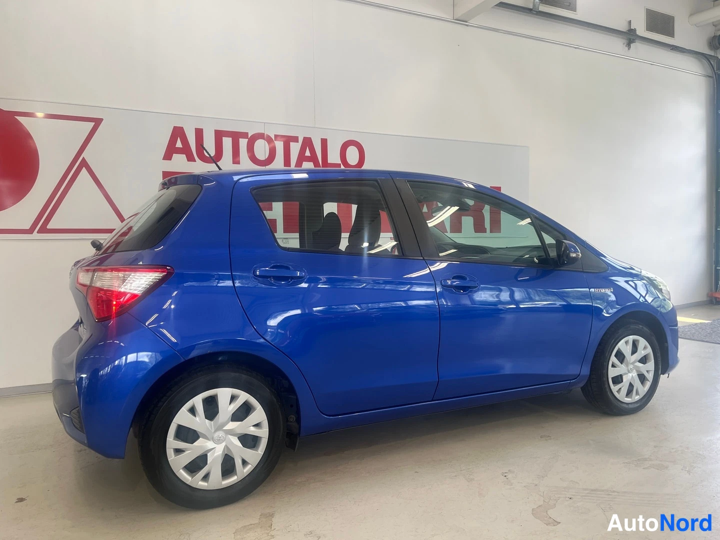 Takaviisto: Takimmainen oikeanpuolinen 3/4-näkymä sininen Toyota Yaris sisätiloissa, takavalot näkyvissä.